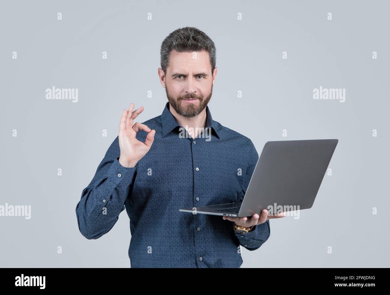 Computer programmer show ring gesture holding portable laptop grey background, OK Stock Photo