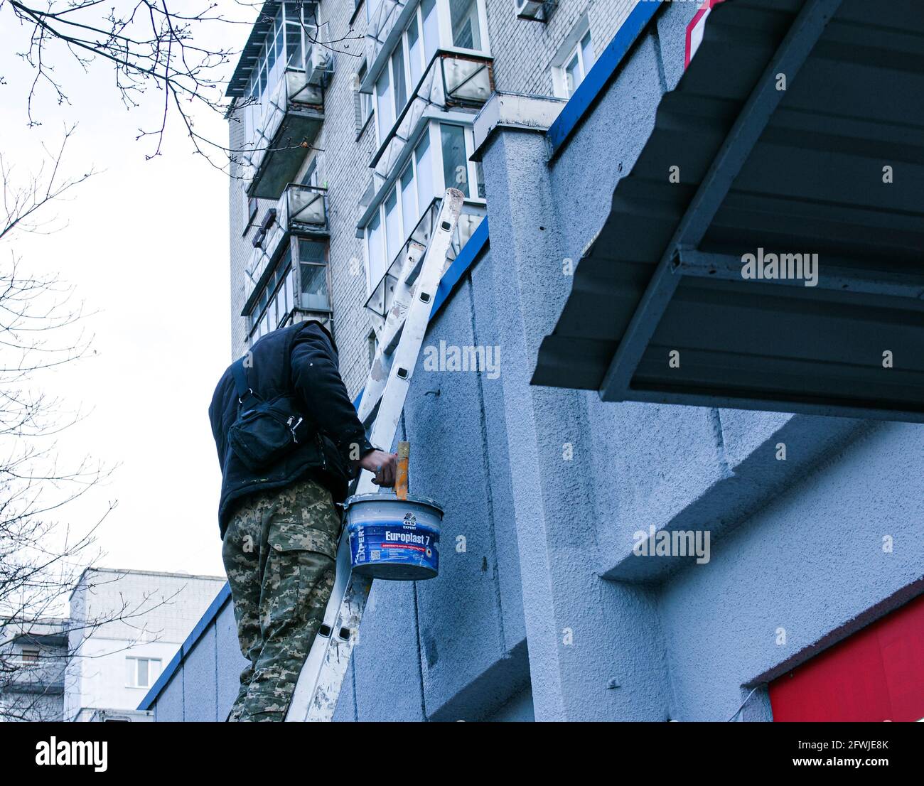 Dnepropetrovsk, Ukraine - 03.29.2021: The work of the painter is on top. An employee paints the facade of a building while standing on the stairs. Stock Photo