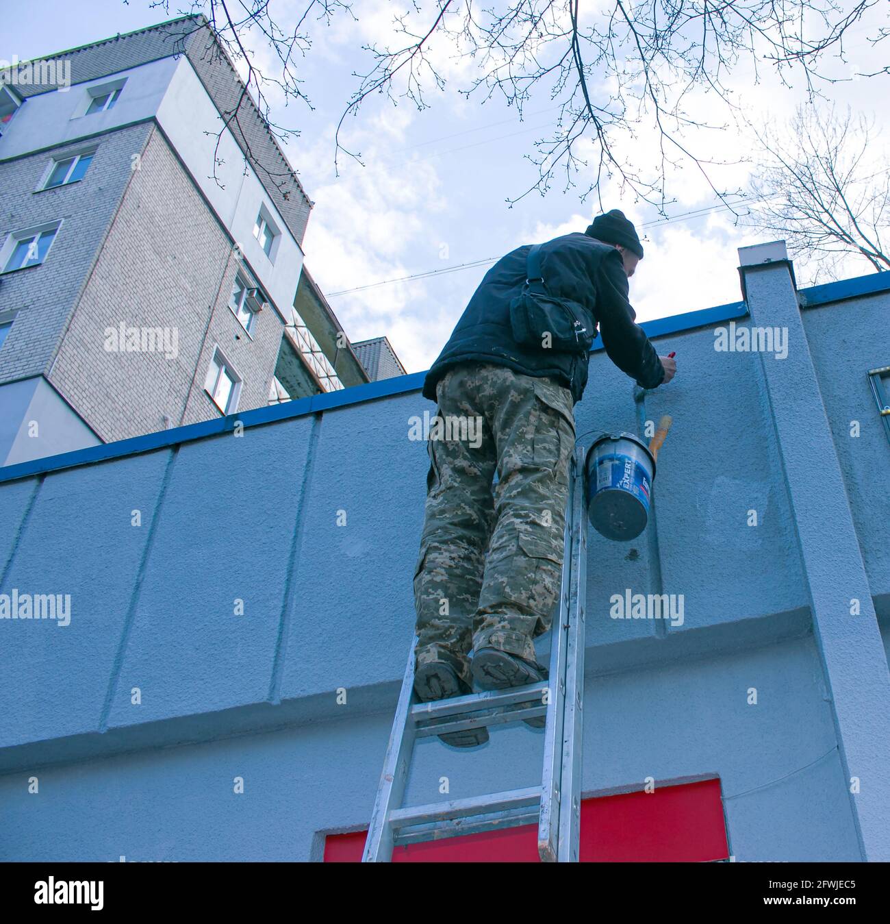 Dnepropetrovsk, Ukraine - 03.29.2021: The work of the painter is on top. An employee paints the facade of a building while standing on the stairs. Stock Photo