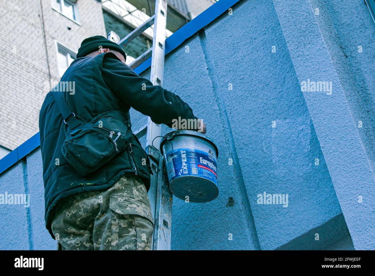 Dnepropetrovsk, Ukraine - 03.29.2021: The work of the painter is on top. An employee paints the facade of a building while standing on the stairs. Stock Photo