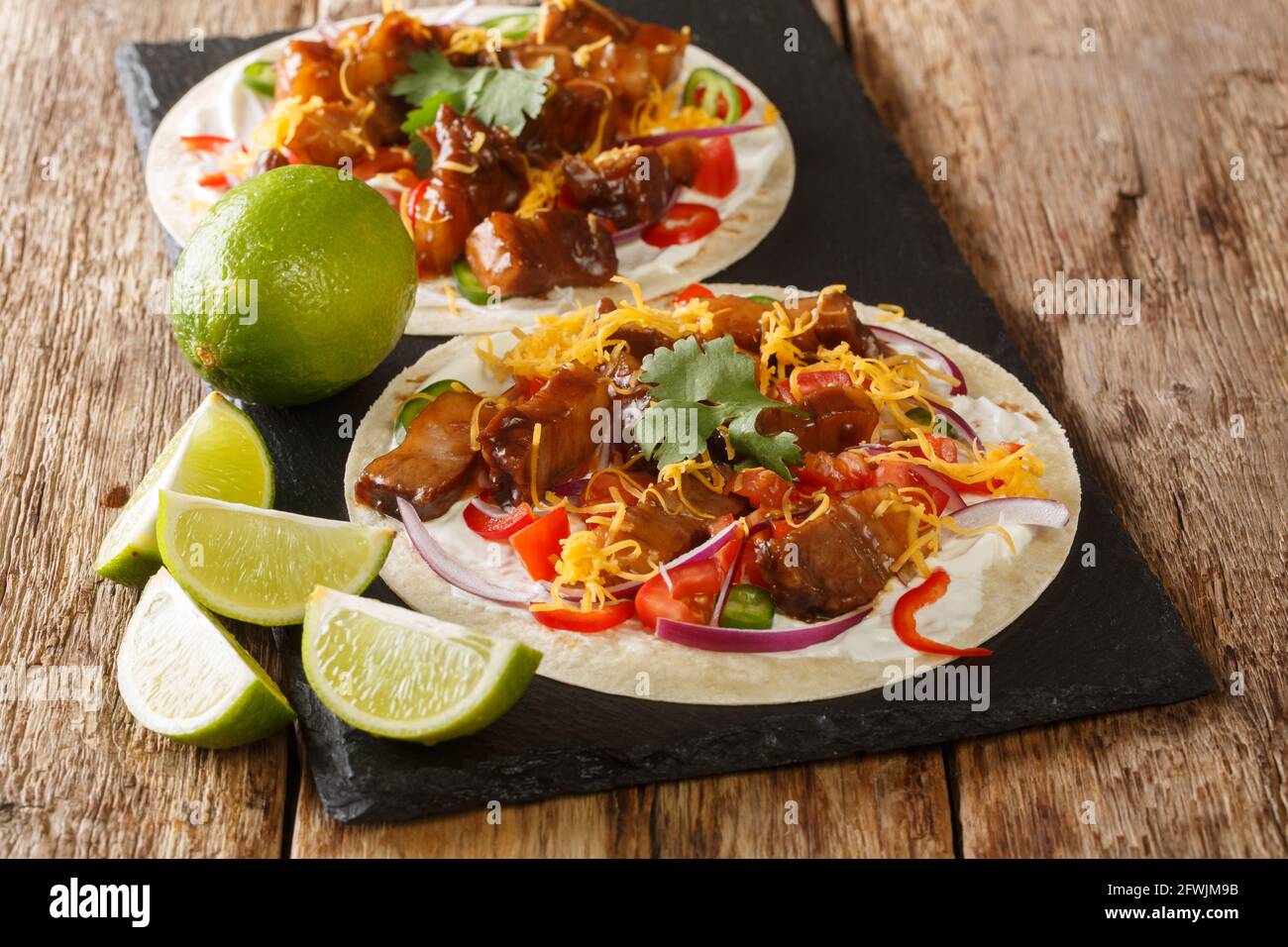 Hot tacos with grilled pork belly, seasonal vegetables, cheddar and lime close-up on a slate board on the table. horizontal Stock Photo