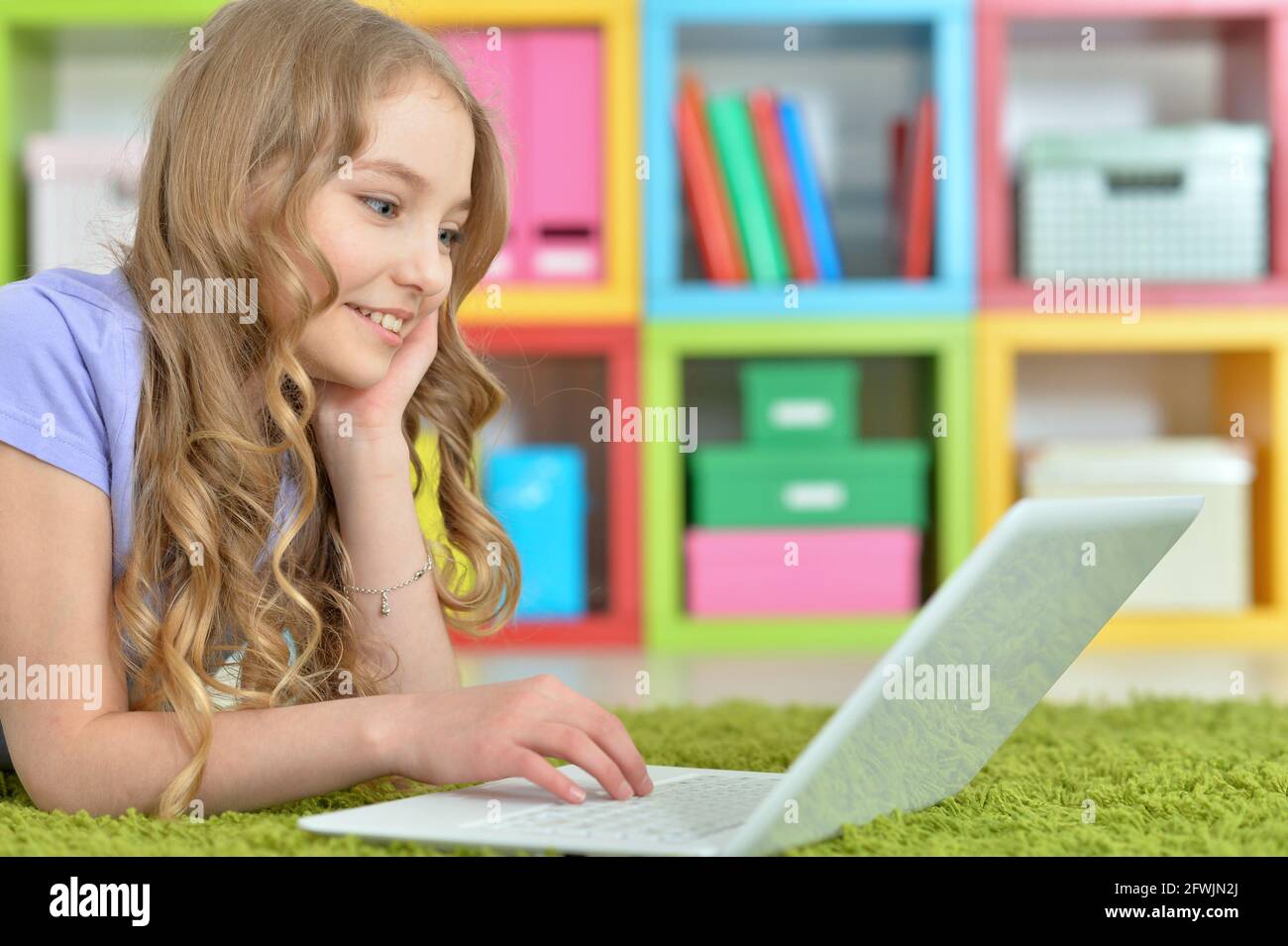 Cute girl using laptop while lying on green floor at home Stock Photo ...