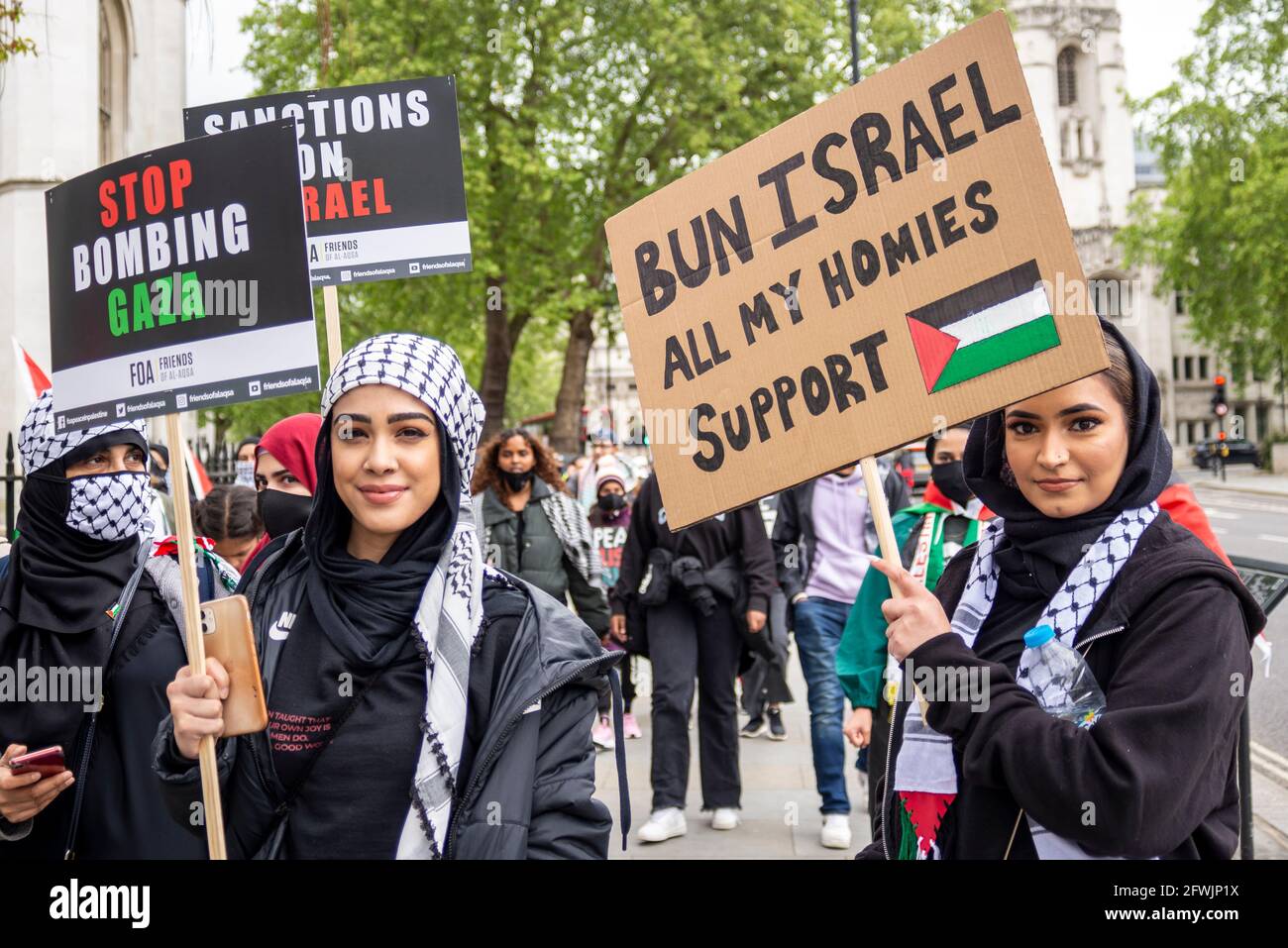 Protesters at a pro Palestine demonstration march in London, UK. Young females with placards, one with bun Israel, all my homies support Palestine Stock Photo