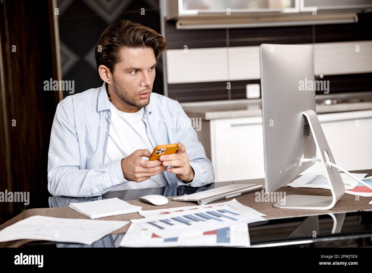 Concentrated male freelancer doing paperwork, sitting at the desk in home office. Focused young businessman or student working or studying distantly Stock Photo
