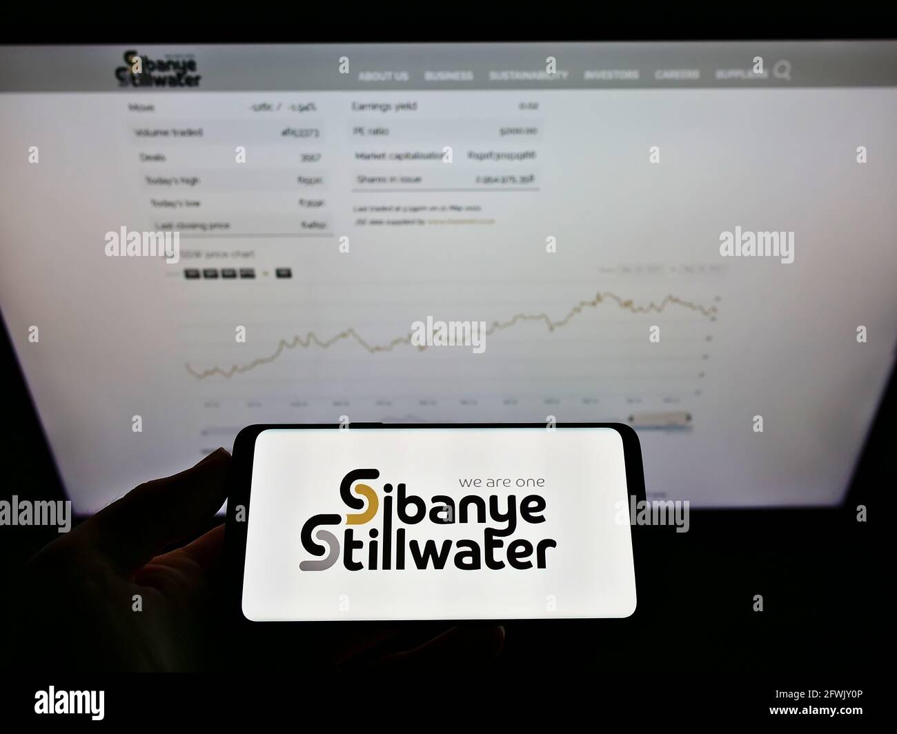 Person holding smartphone with logo of South African mining company Sibanye Stillwater Limited on screen in front of webpage. Focus on phone display. Stock Photo