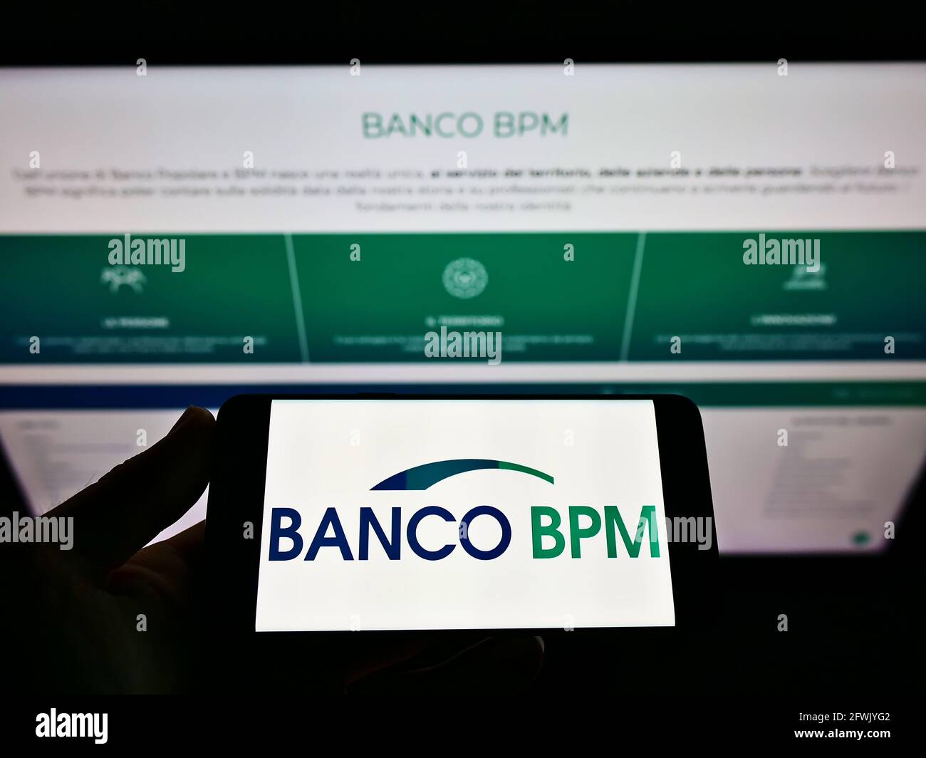 High angle view of person holding smartphone with logo of Italian Bank Banco BPM SpA on screen in front of business web page. Focus on phone display. Stock Photo