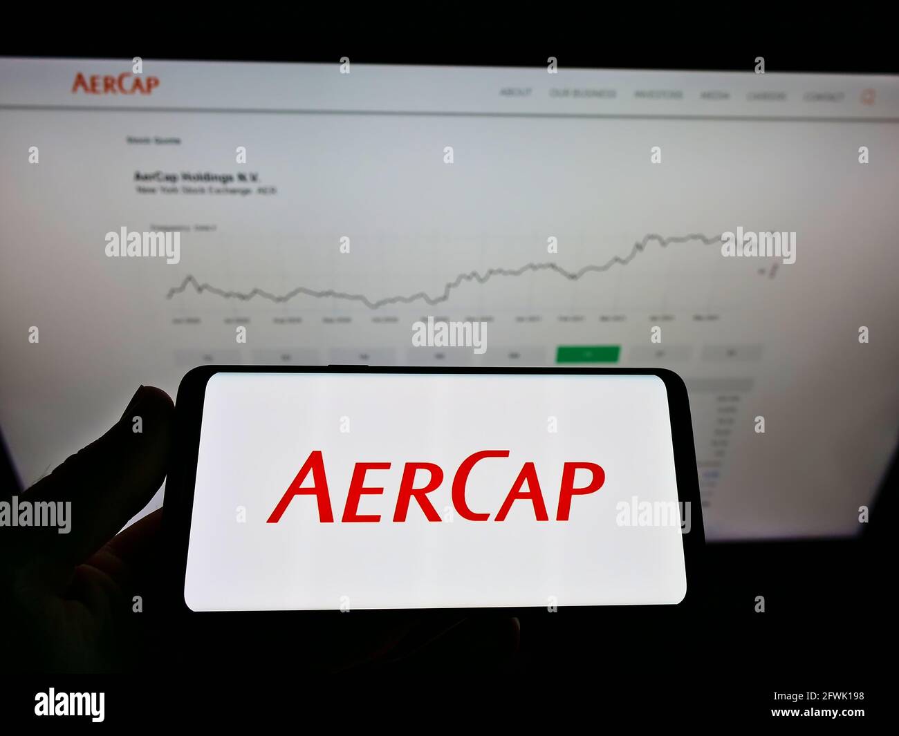 Person holding cellphone with logo of aircraft leasing company AerCap Holdings N.V. on screen in front of website with chart. Focus on phone display. Stock Photo