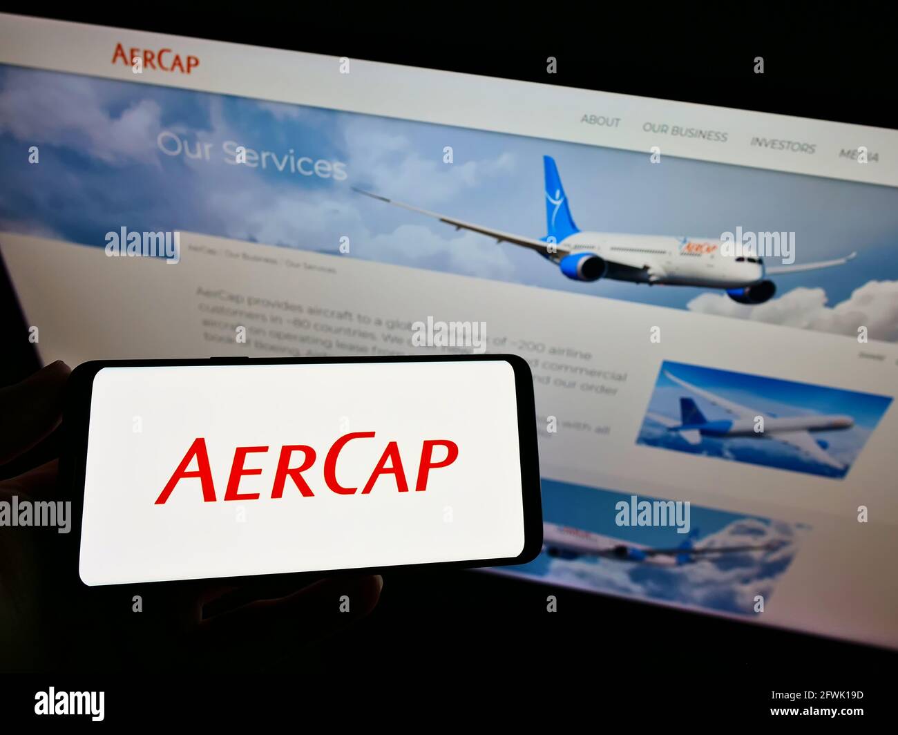 Person holding mobile phone with logo of aircraft leasing company AerCap Holdings N.V. on screen in front of webpage. Focus on phone display. Stock Photo