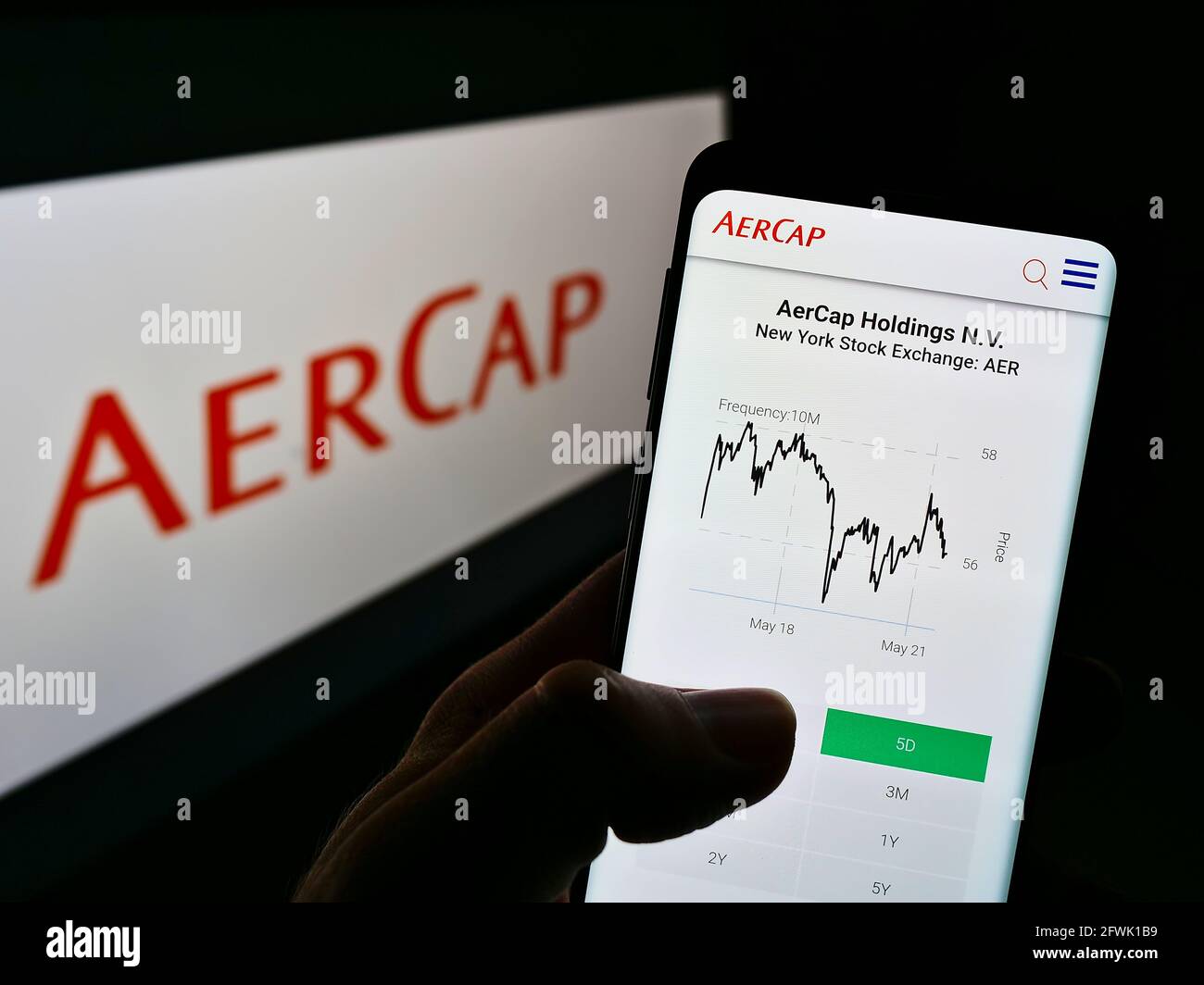 Person holding mobile phone with website of aircraft leasing company AerCap Holdings NV on screen in front of logo. Focus on center of phone display. Stock Photo