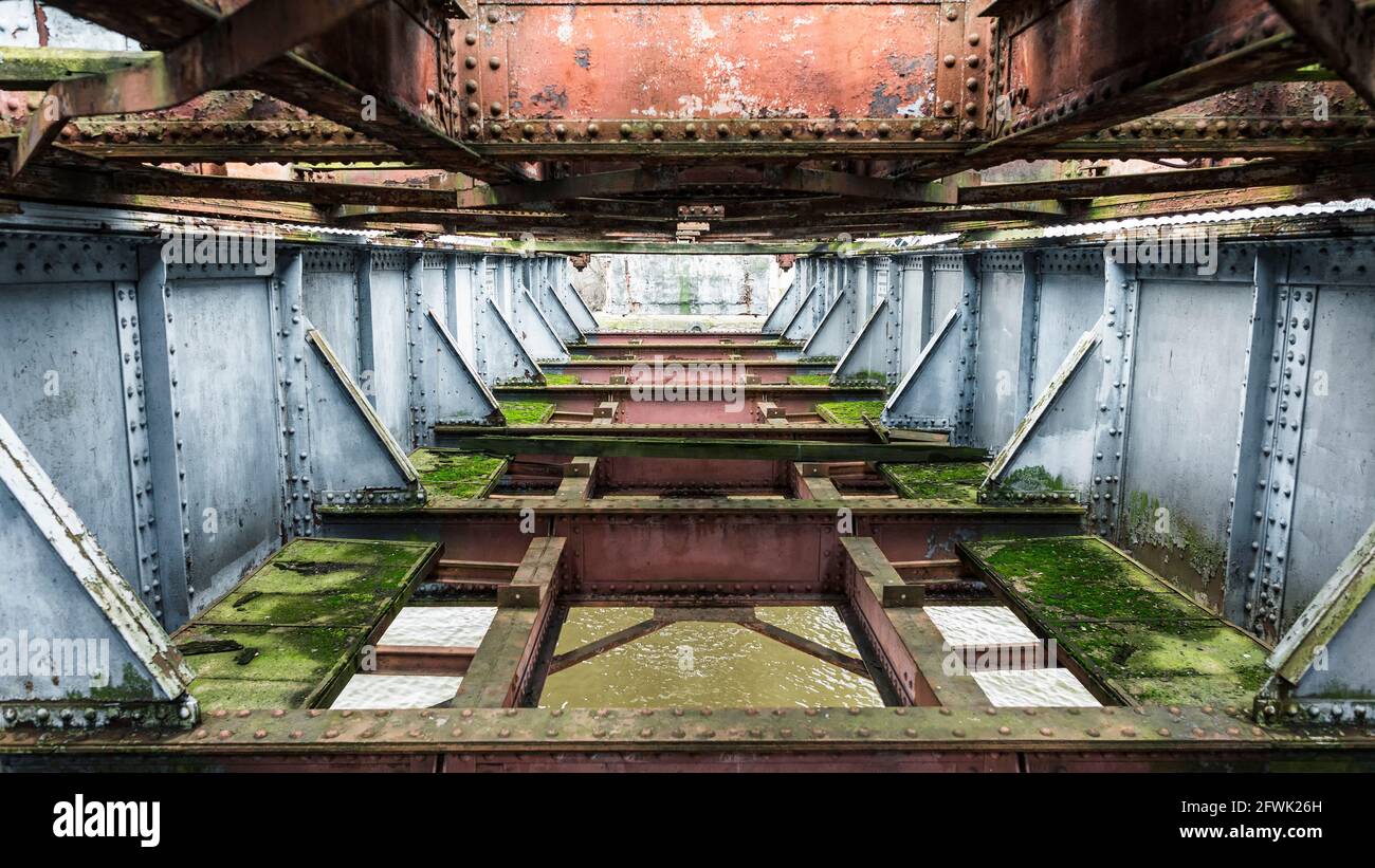 Rusted metal structure of an old railway bridge, covered with moss Stock Photo