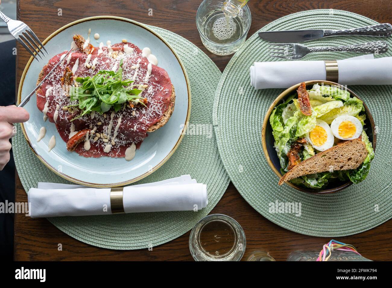 Eating out, top down view of lunch with ceasar salad and beef carpaccio sandwich in luxury lunch space, green placemats and white napkins Stock Photo