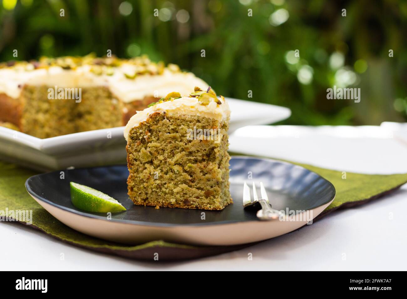 Lime and pastachio cake in garden setting with a slice of cake and lime in foreground Stock Photo