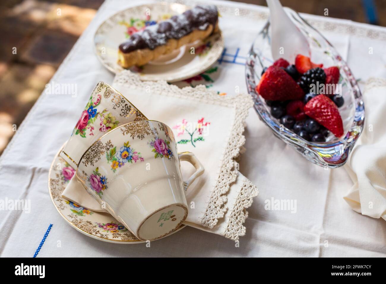Outdoor afternoon tea setting, tea cups, fruit and choclate eclair Stock Photo