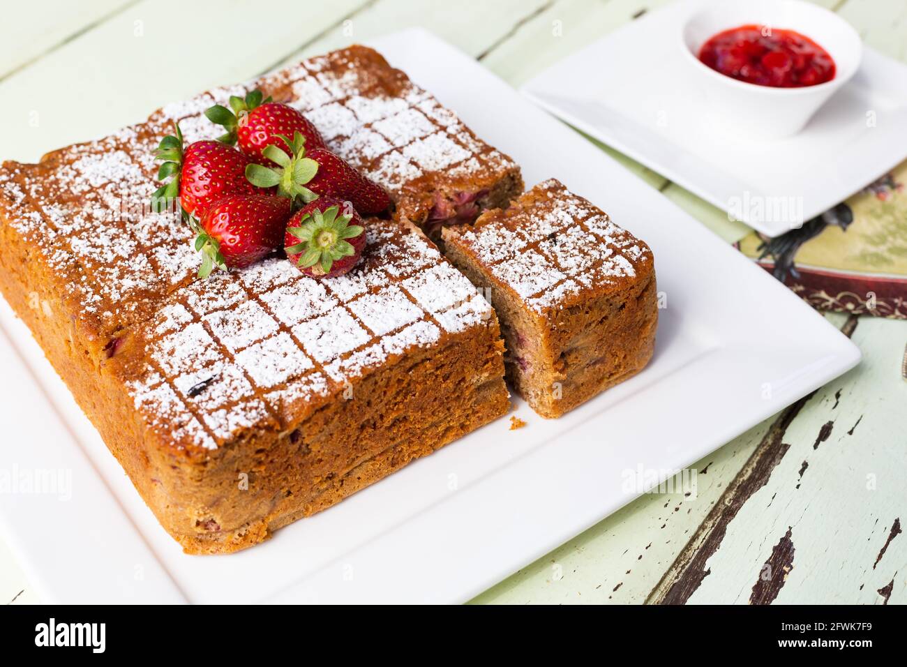 Square cake with cut slice on white plate with strawberries on top and couli on the side Stock Photo