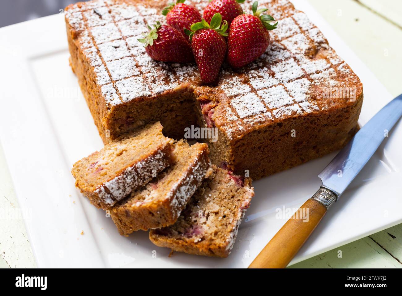 Square cake with slices and knife on white plate with strawberries on top Stock Photo