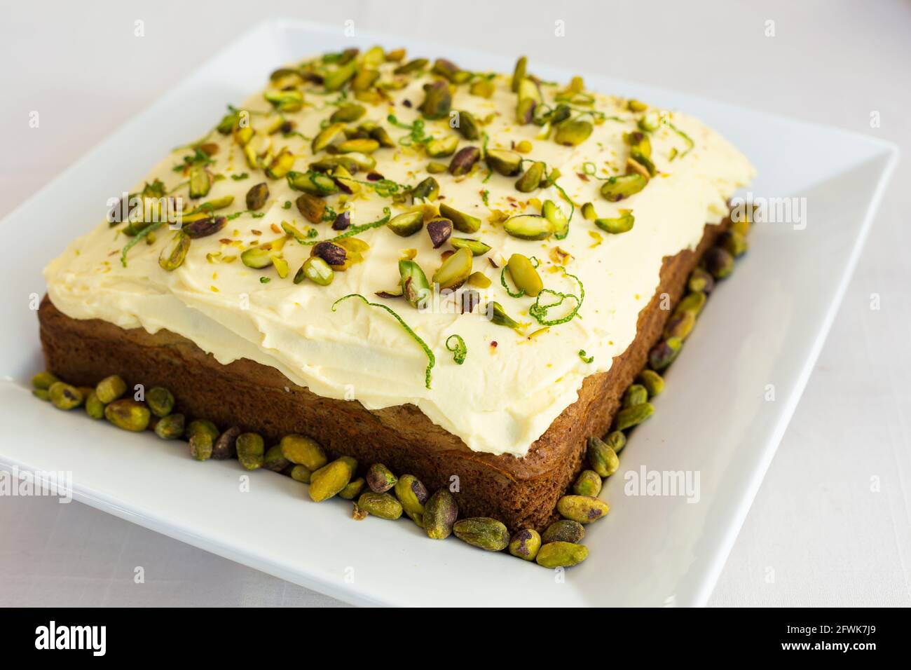 Square lime and pistachio cake on white platter decorated with lime peel and pistachios Stock Photo