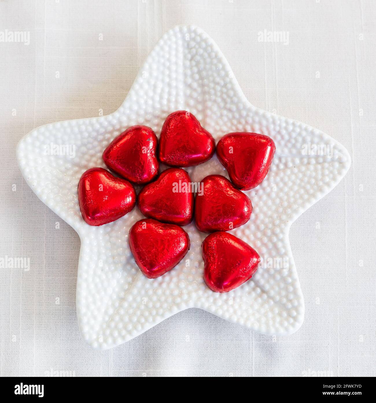 White dimpled plate with red heart shaped chocolates Stock Photo