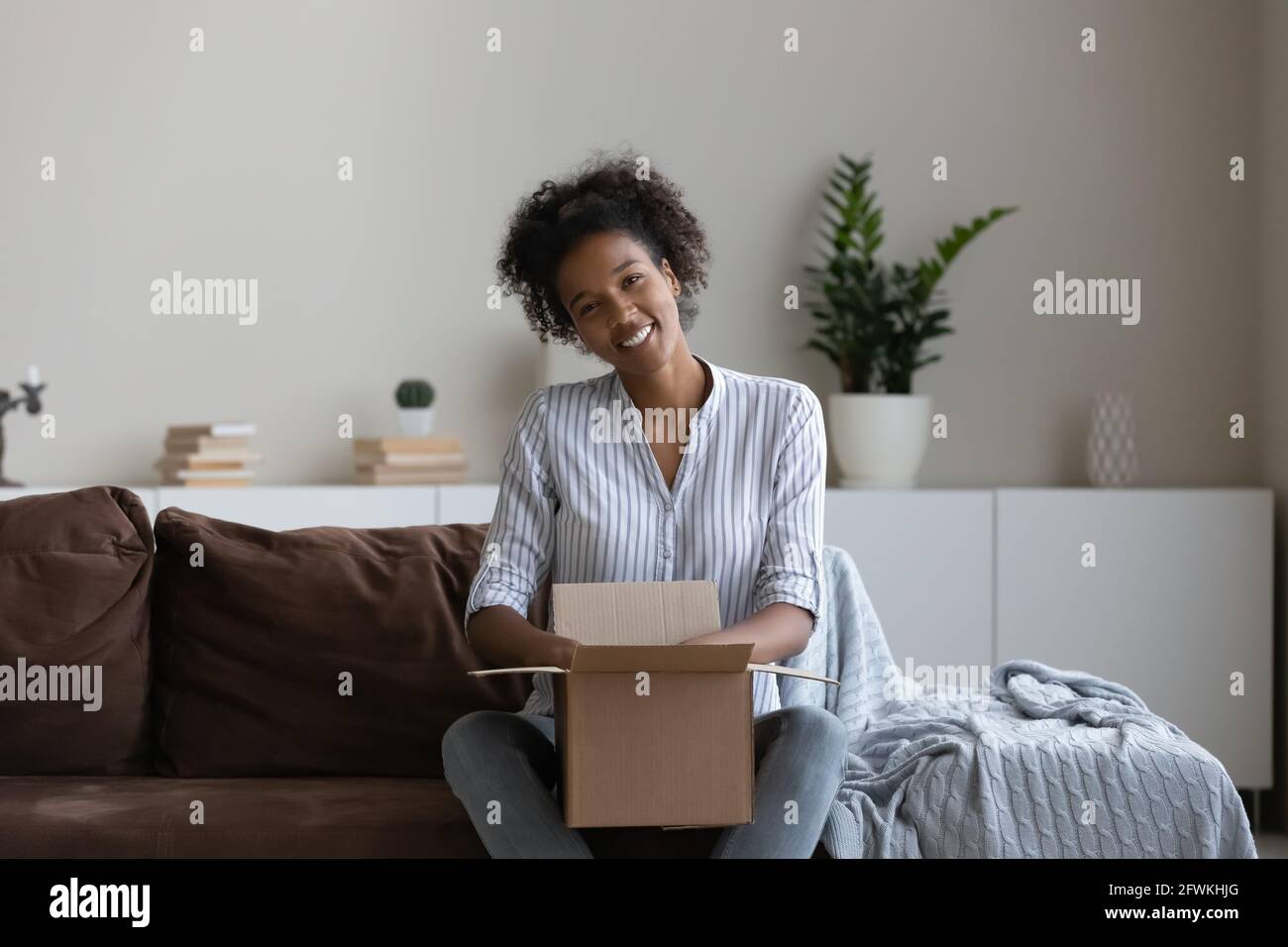 Portrait of happy sincere young african woman with carton parcel. Stock Photo