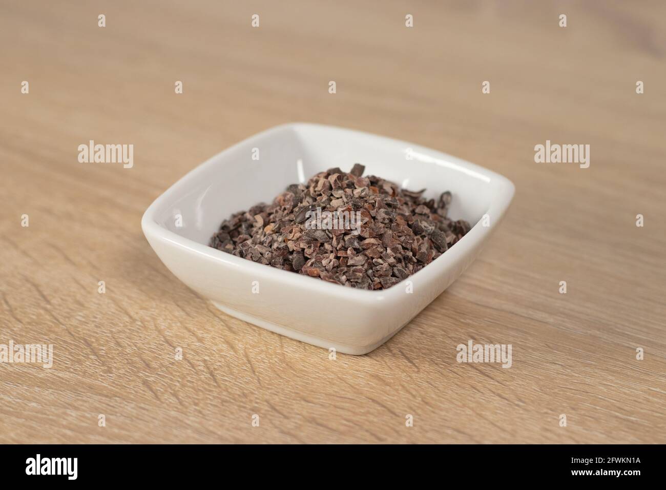 Roasted ground cacao bean on a white square bowl. Cacao Nibs. Stock Photo
