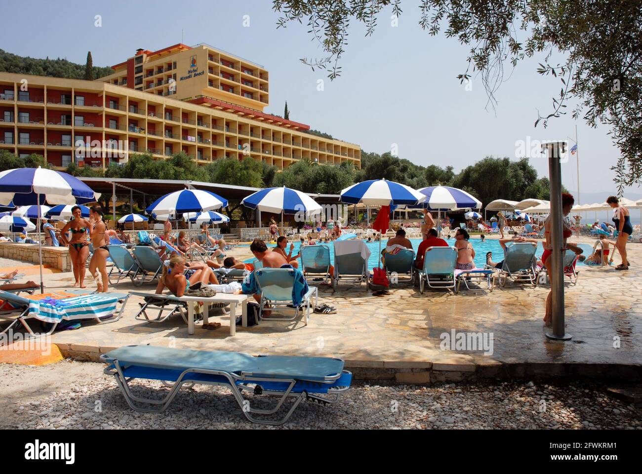 Holidaymakers sitting round the hotel swimming pool relaxing and enjoying the hot sunshine, Nissaki Beach, Corfu, Greece Stock Photo