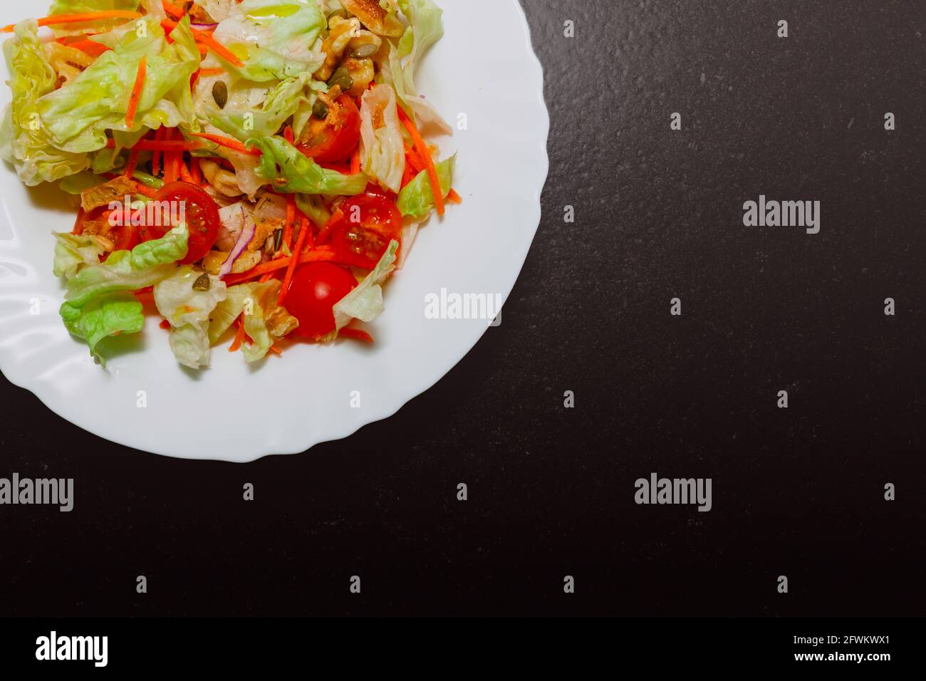 There is a salad plate in a corner of the picture, part of the plate is hidden. The ingredients are: lettuce, cherry tomato, carrot, walnuts, and pump Stock Photo