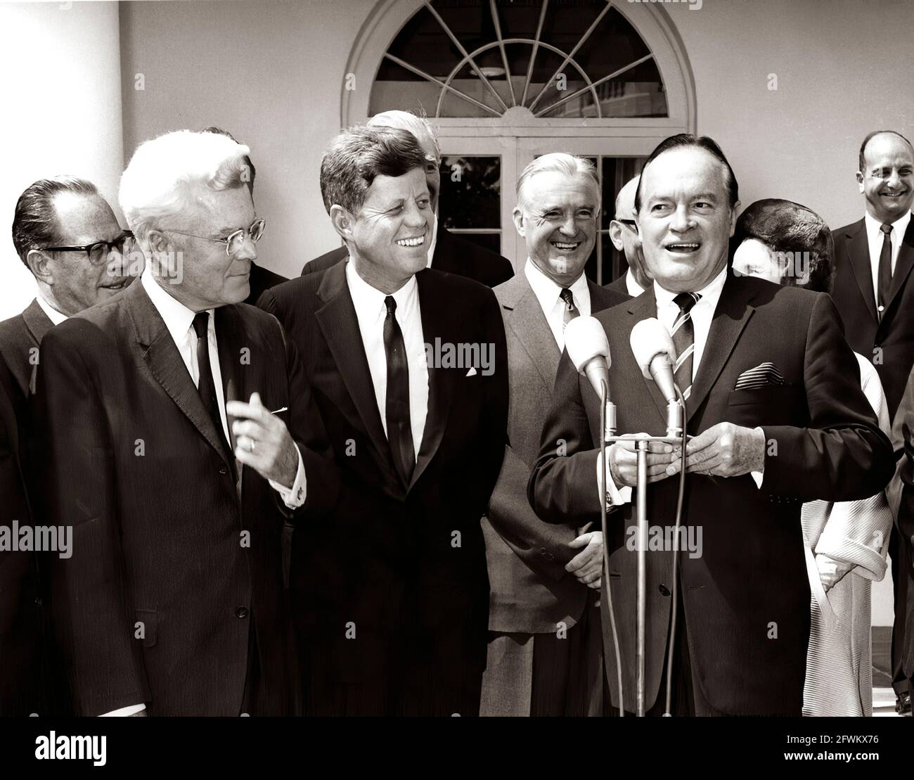 President John F. Kennedy laughs as actor and comedian, Bob Hope, delivers remarks after receiving the Congressional Gold Medal, presented by President Kennedy in recognition of his services to the country as an entertainer during World War II. Left to right: Senator Thomas H. Kuchel (California); Representative Michael A. Feighan (Ohio); President Kennedy; Senator Stuart Symington (Missouri); Mr. Hope; Dolores Hope (mostly hidden), wife of Mr. Hope; unidentified man. Rose Garden, White House, Washington, D.C. Stock Photo