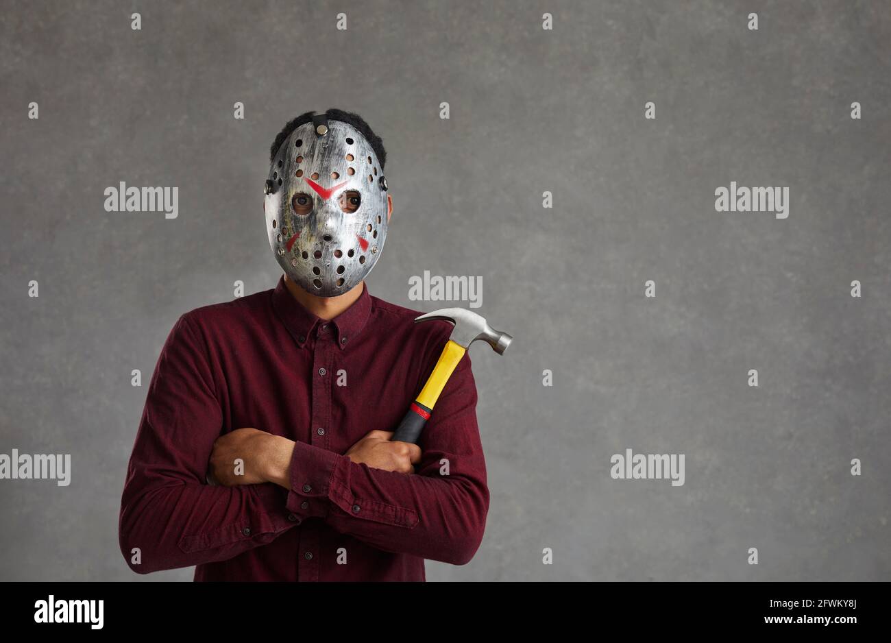 Studio portrait of an unknown man on a gray background who is dressed in a spooky maniac mask. Stock Photo