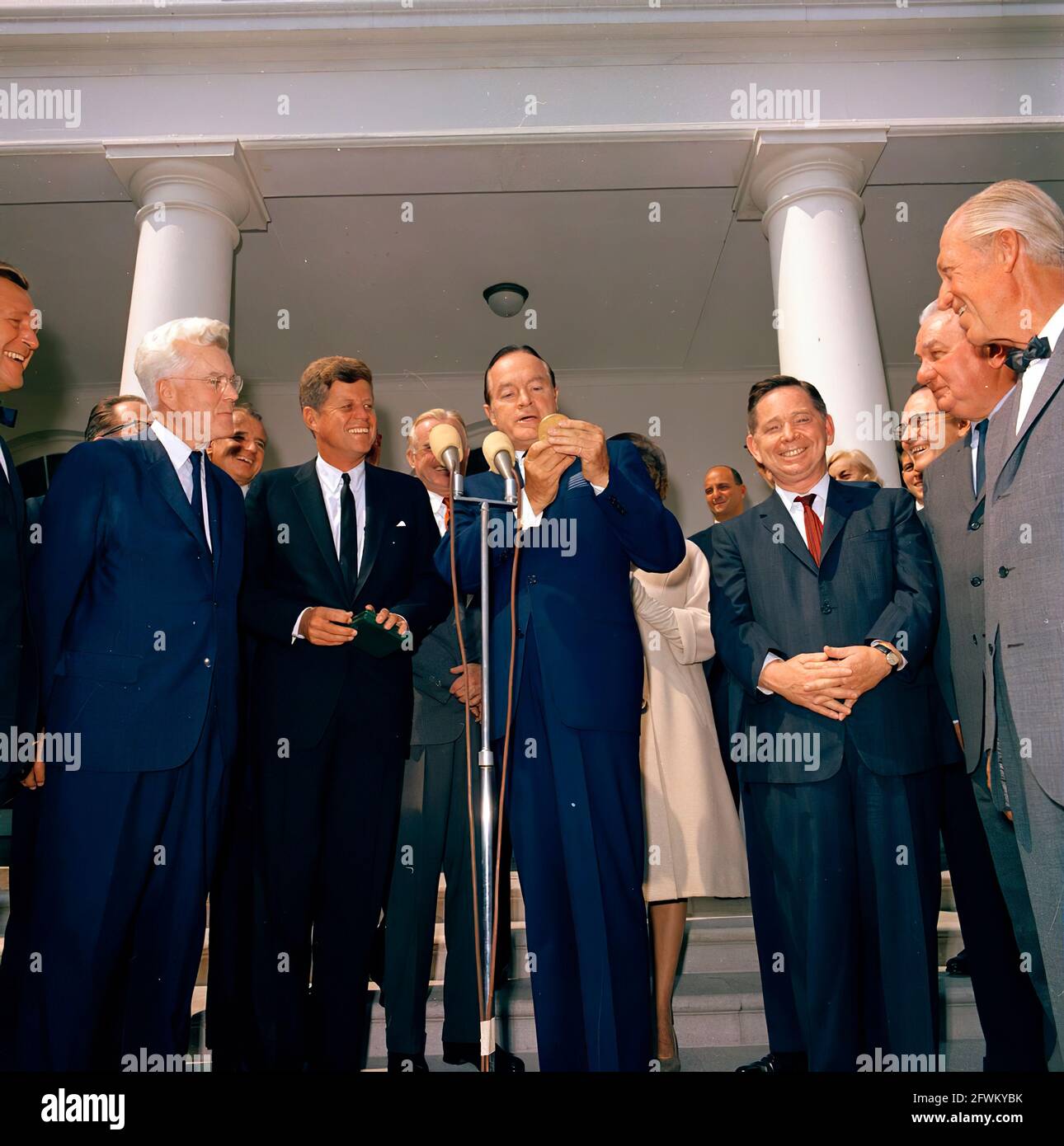 Actor and comedian, Bob Hope, delivers remarks after receiving the Congressional Gold Medal, presented by President John F. Kennedy in recognition of his services to the country as an entertainer during World War II. Left to right: unidentified; Representative Michael A. Feighan (Ohio); President Kennedy; Mr. Hope’s wife, Dolores Hope; Mr. Hope; unidentified (behind Mr. Hope); Senator Stuart Symington (Missouri); Representative Carl Albert (Oklahoma); Representative Leslie C. Arends (Illinois). Also pictured (standing at left, in background): Naval Aide to the President, Captain Shepard. Stock Photo