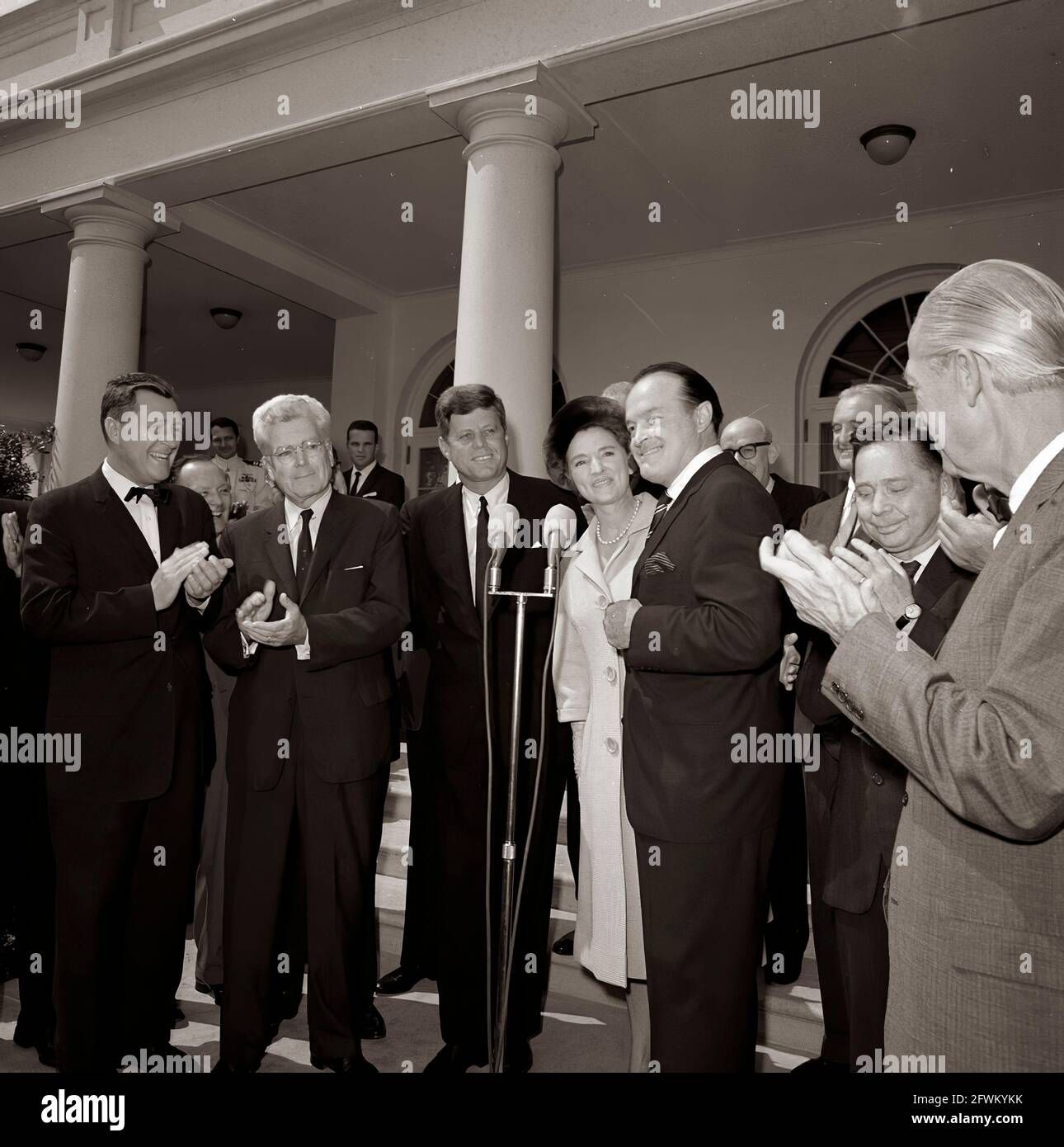Actor and comedian, Bob Hope, delivers remarks after receiving the Congressional Gold Medal, presented by President John F. Kennedy in recognition of his services to the country as an entertainer during World War II. Left to right: unidentified; Representative Michael A. Feighan (Ohio); President Kennedy; Mr. Hope’s wife, Dolores Hope; Mr. Hope; unidentified (behind Mr. Hope); Senator Stuart Symington (Missouri); Representative Carl Albert (Oklahoma); Representative Leslie C. Arends (Illinois). Also pictured (standing at left, in background): Naval Aide to the President, Captain Shepard. Stock Photo