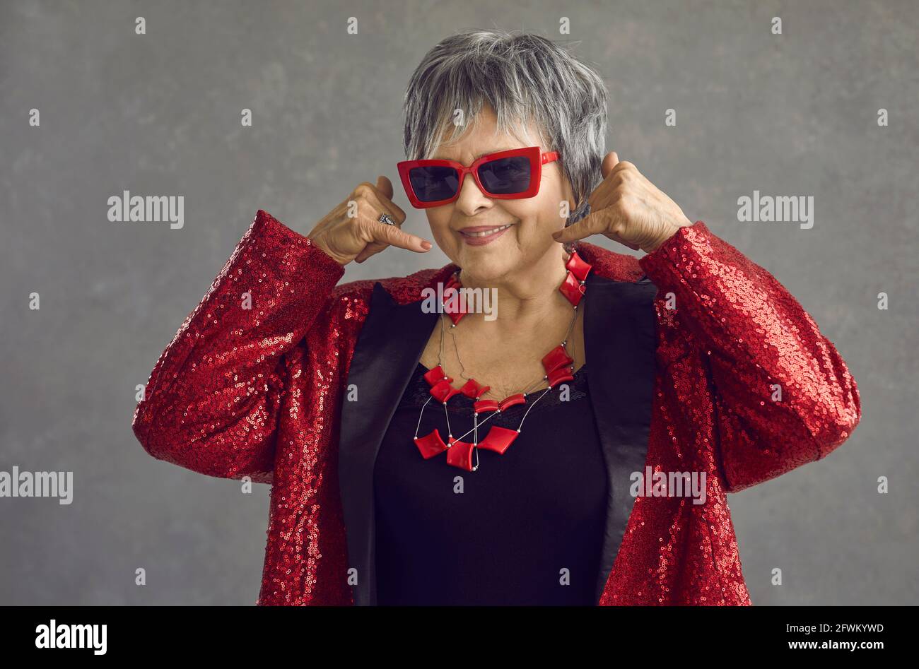 Headshot studio portrait of trendy fashion old woman showing call me gesture Stock Photo