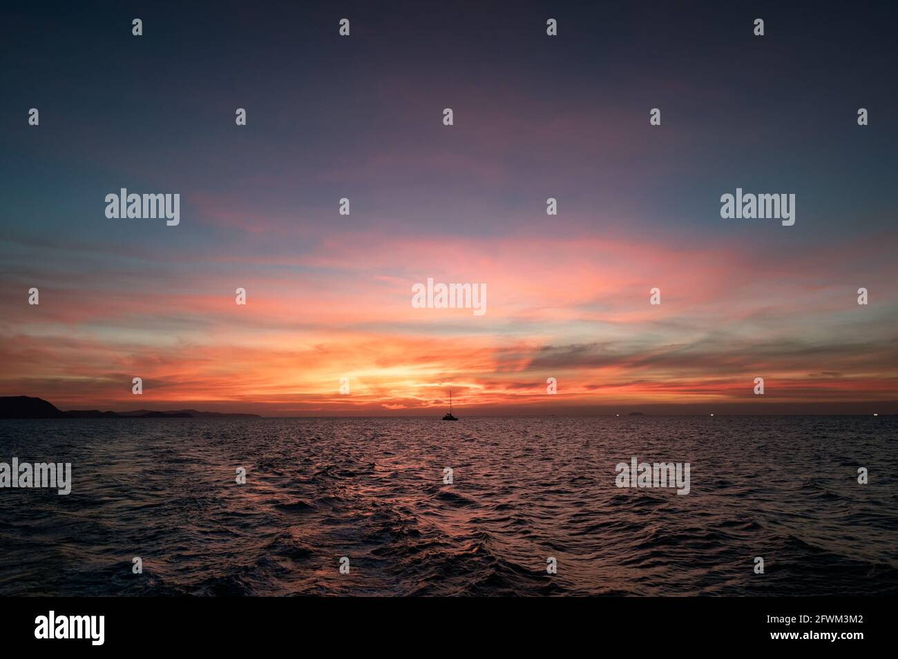 Beautiful sunset sky over tropical sea and boat sailing in the evening ...