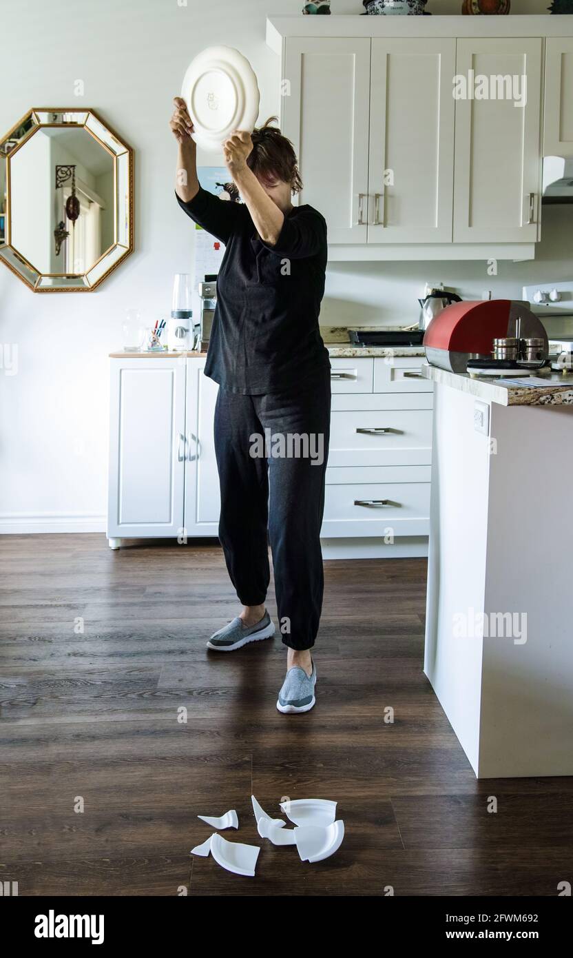 Mature woman revolting and breaking some dishes in her kitchen. Stock Photo