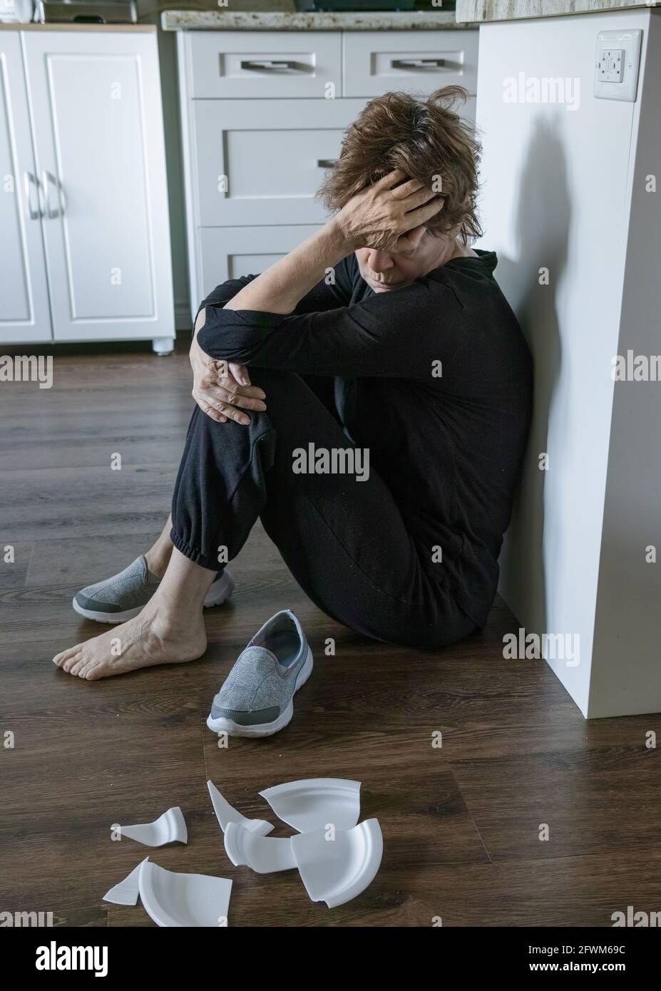 Mature woman in pain, squatting, she broke some dishes. She lost one shoe. Stock Photo