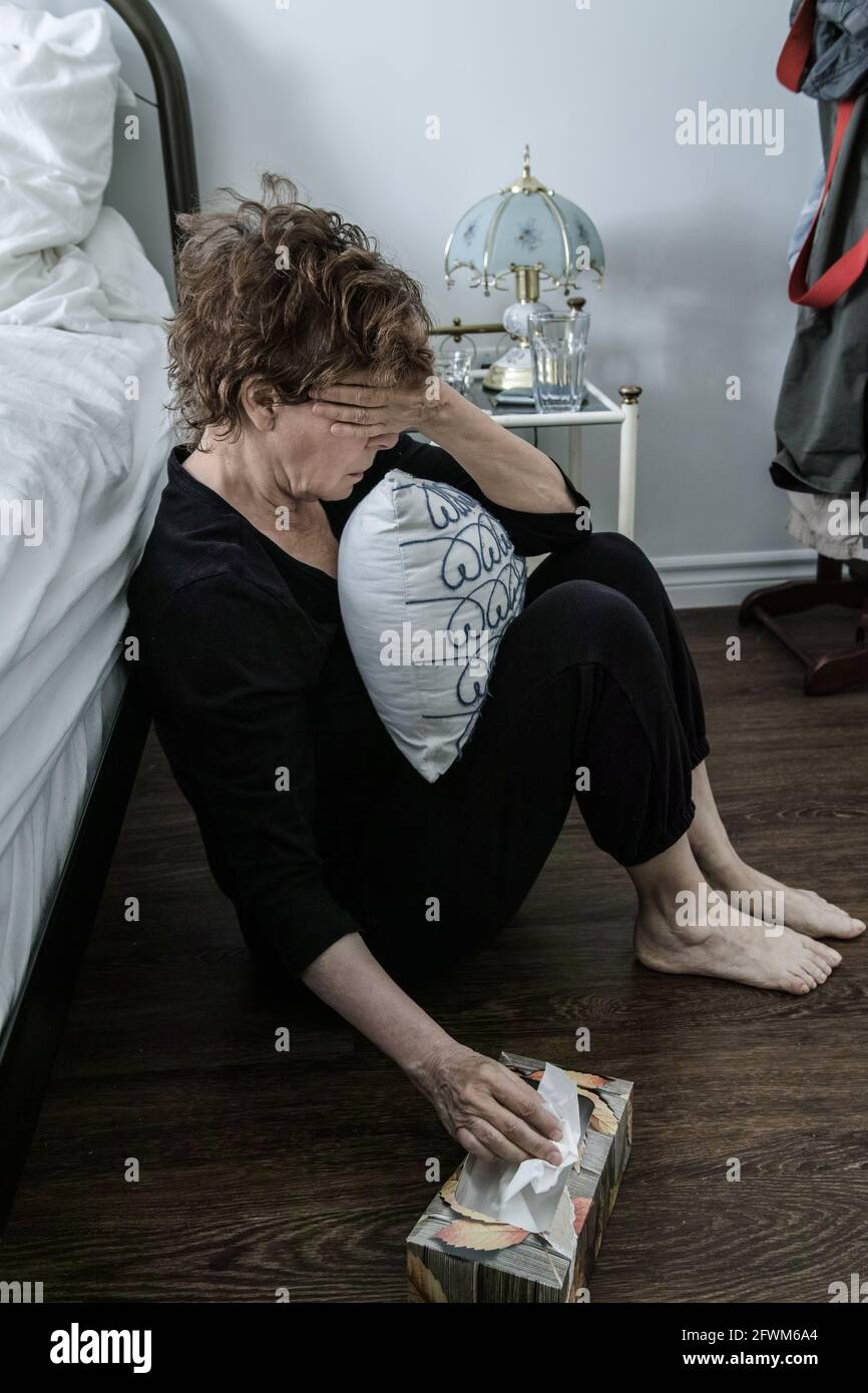 Mature woman in pain, she is squatting and she firmly holds a cushion. She's picking up a tissue Stock Photo