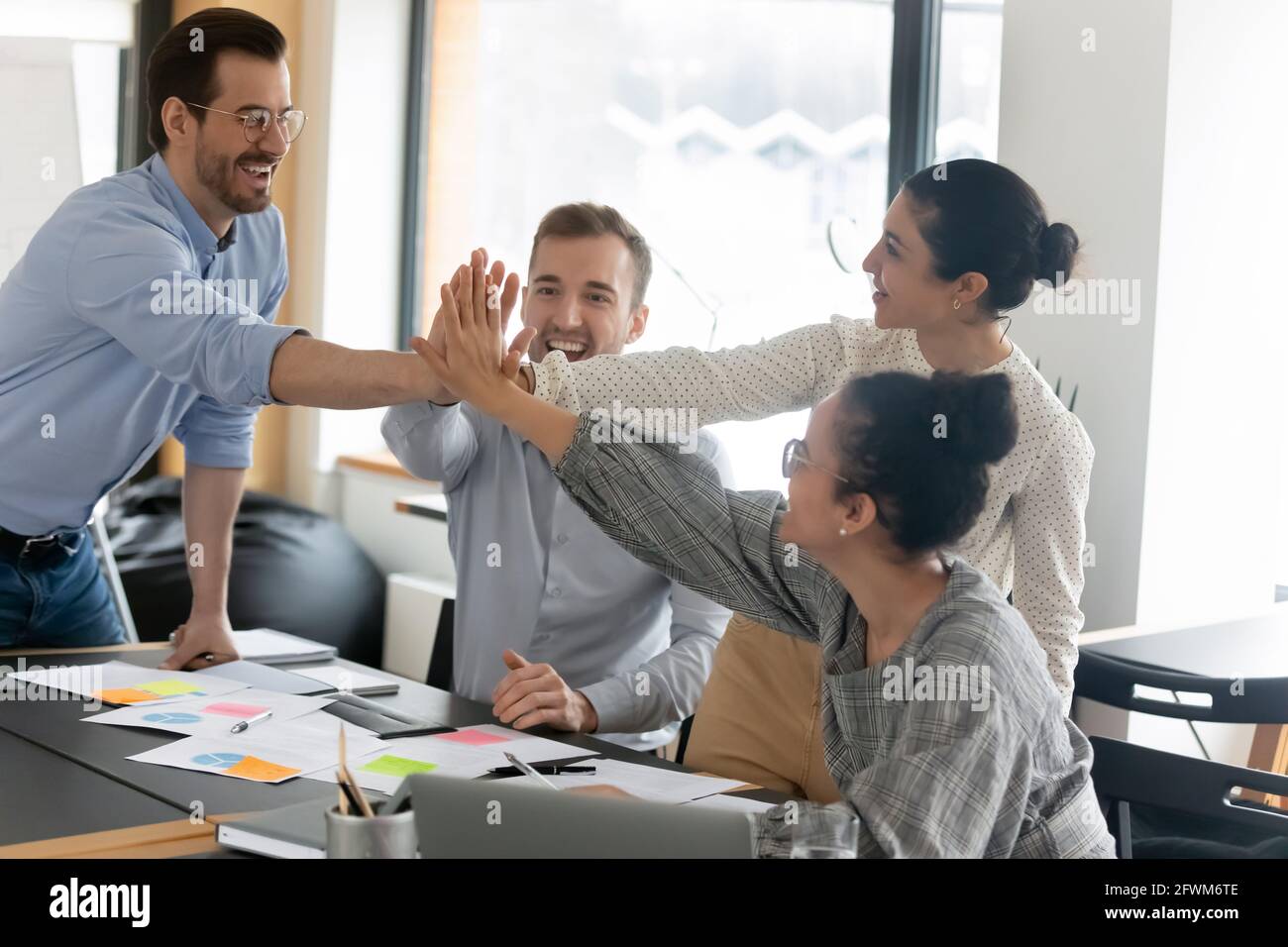 Excited diverse colleagues giving high five at meeting, celebrating ...