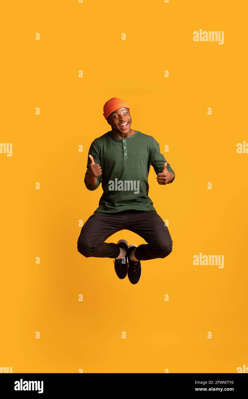 Joyful Black Hipster Guy Jumping In Air And Showing Thumbs Up Stock