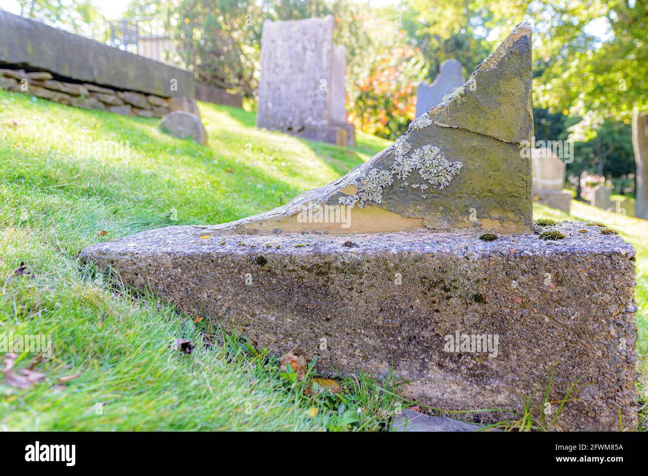 An old broken tombstone on the side of a small hill in a cemetery. Only a small part of the bottom of the grave marker remains. Closeup view. Stock Photo
