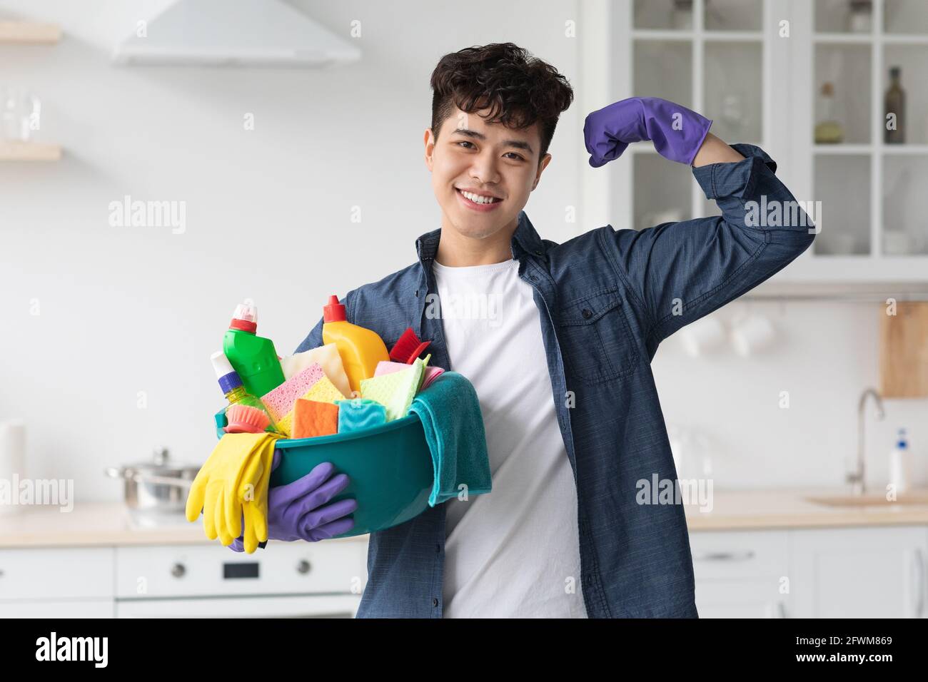 Positive asian guy with cleaning supplies showing muscles Stock Photo
