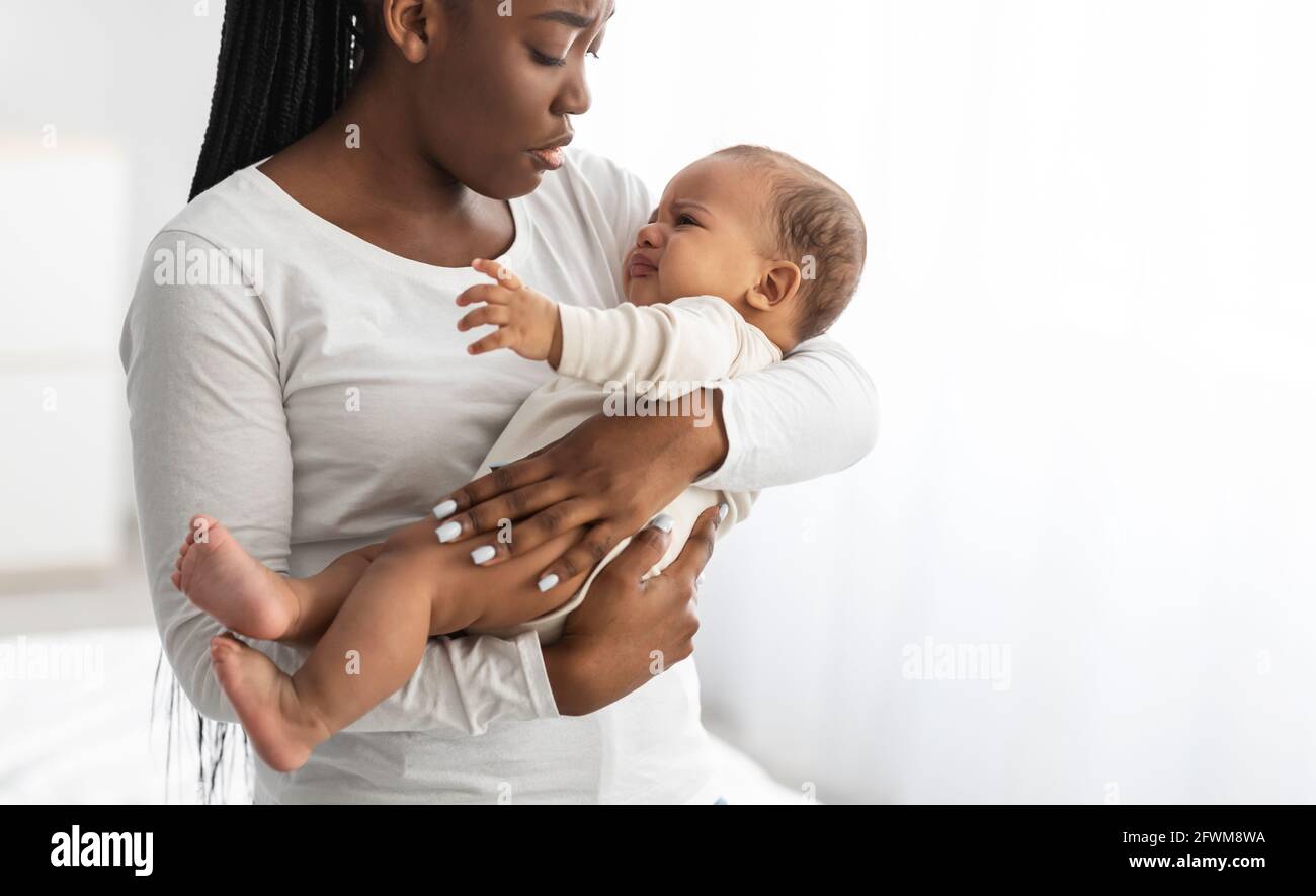 Black mother holding crying baby with colic on hands Stock Photo