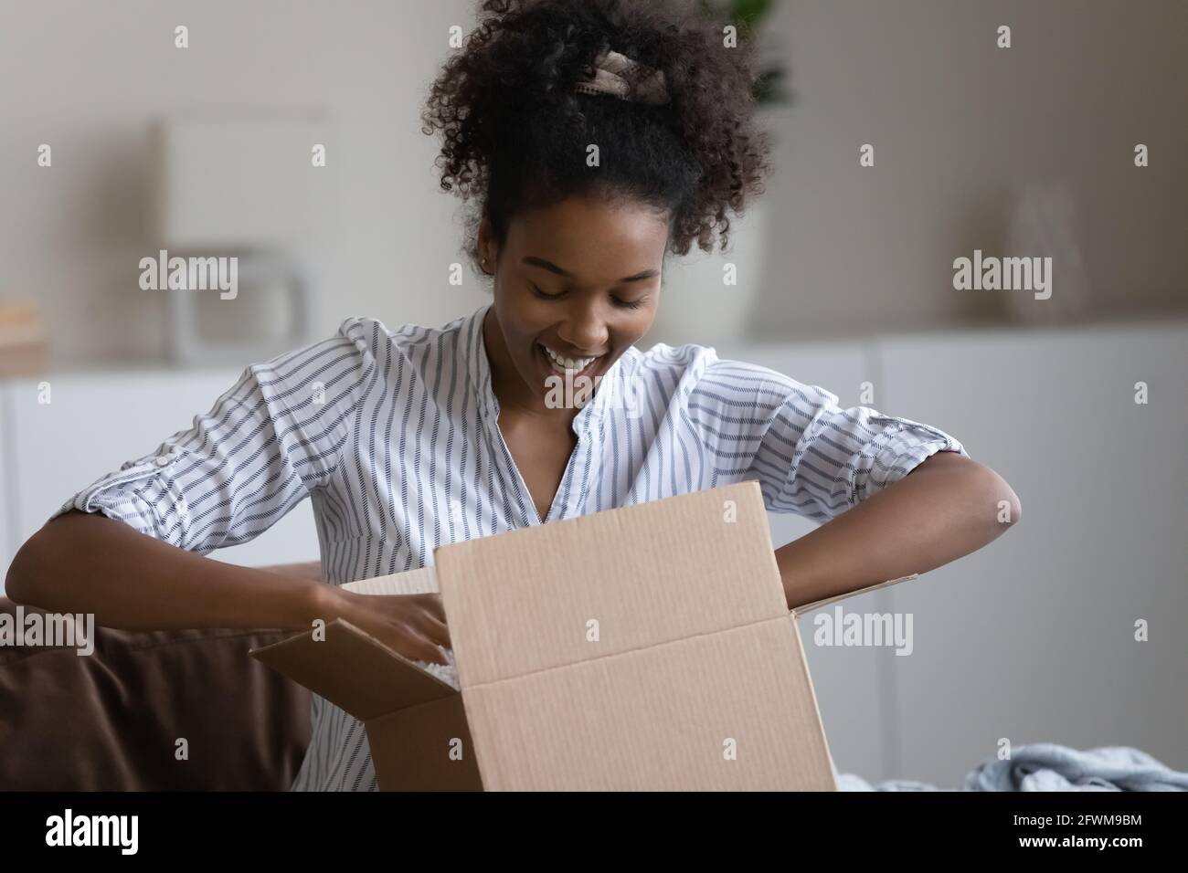 Happy millennial african american woman unpacking parcel. Stock Photo