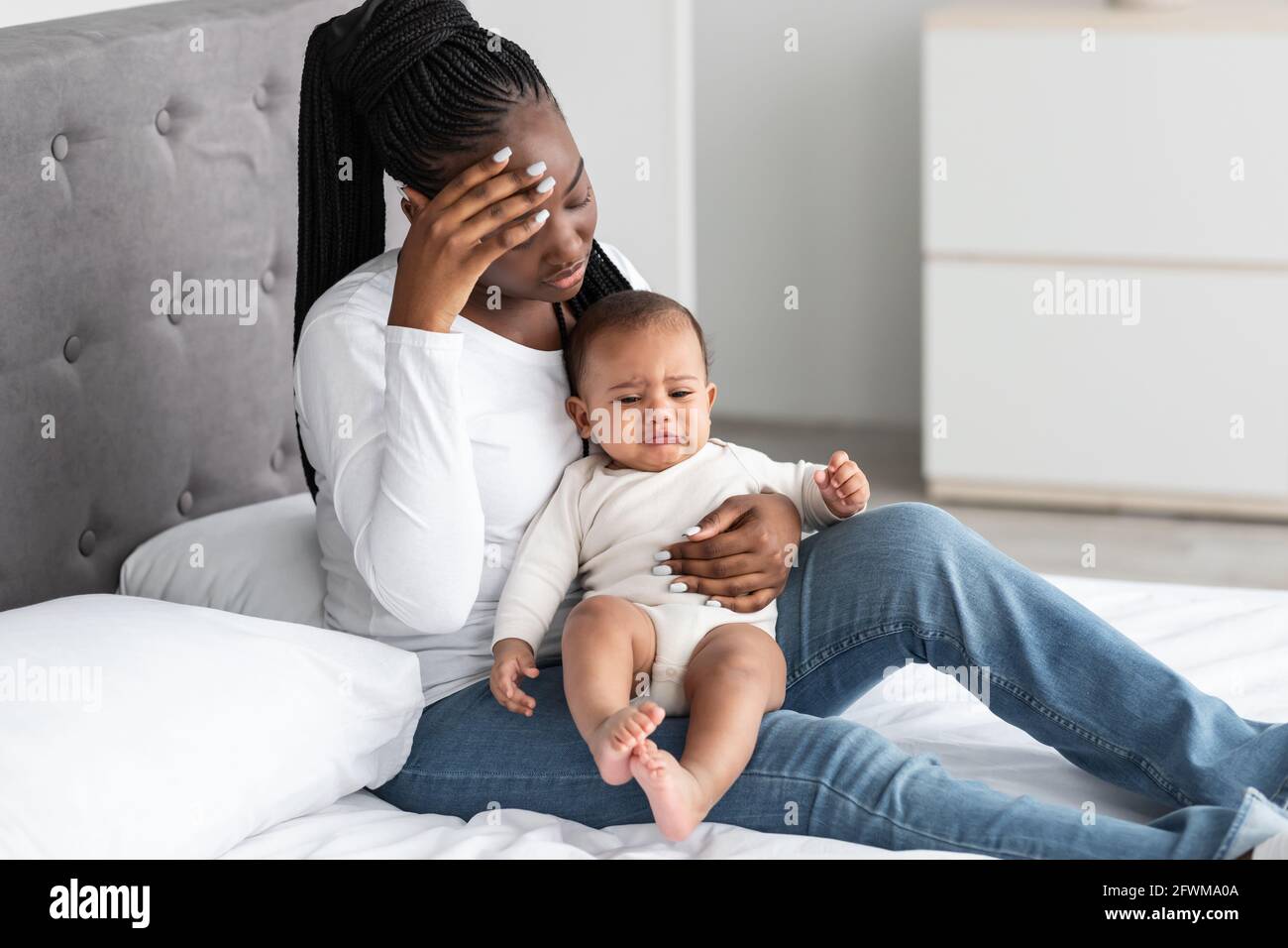 Tired African American young mom sitting with kid on bed Stock Photo