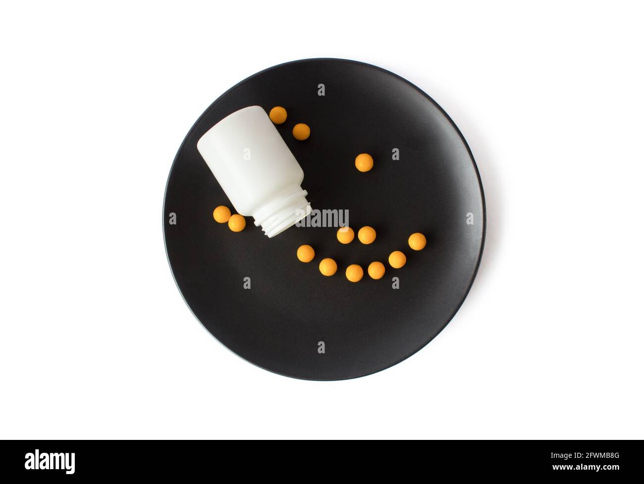 Yellow vitamins pills on a black plate on a white isolated background. Breakfast pills. Stock Photo
