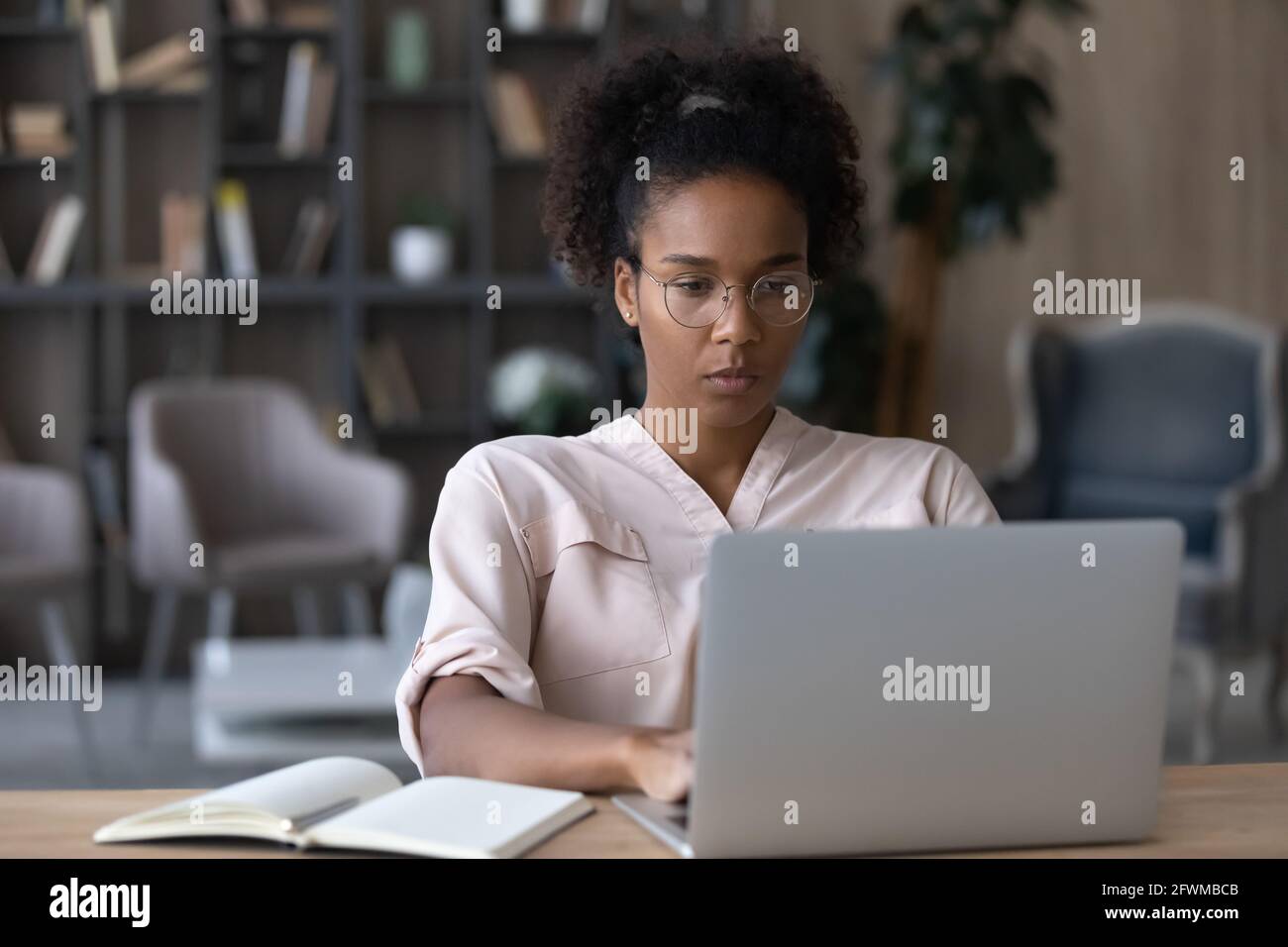 Concentrated young african woman in eyeglasses working on computer. Stock Photo