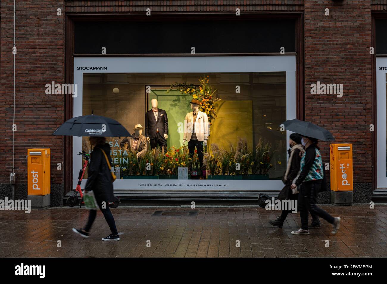 People with umbrellas passing Stockmann department store window display markting summer clothes on a rainy day in Helsinki, Finland Stock Photo