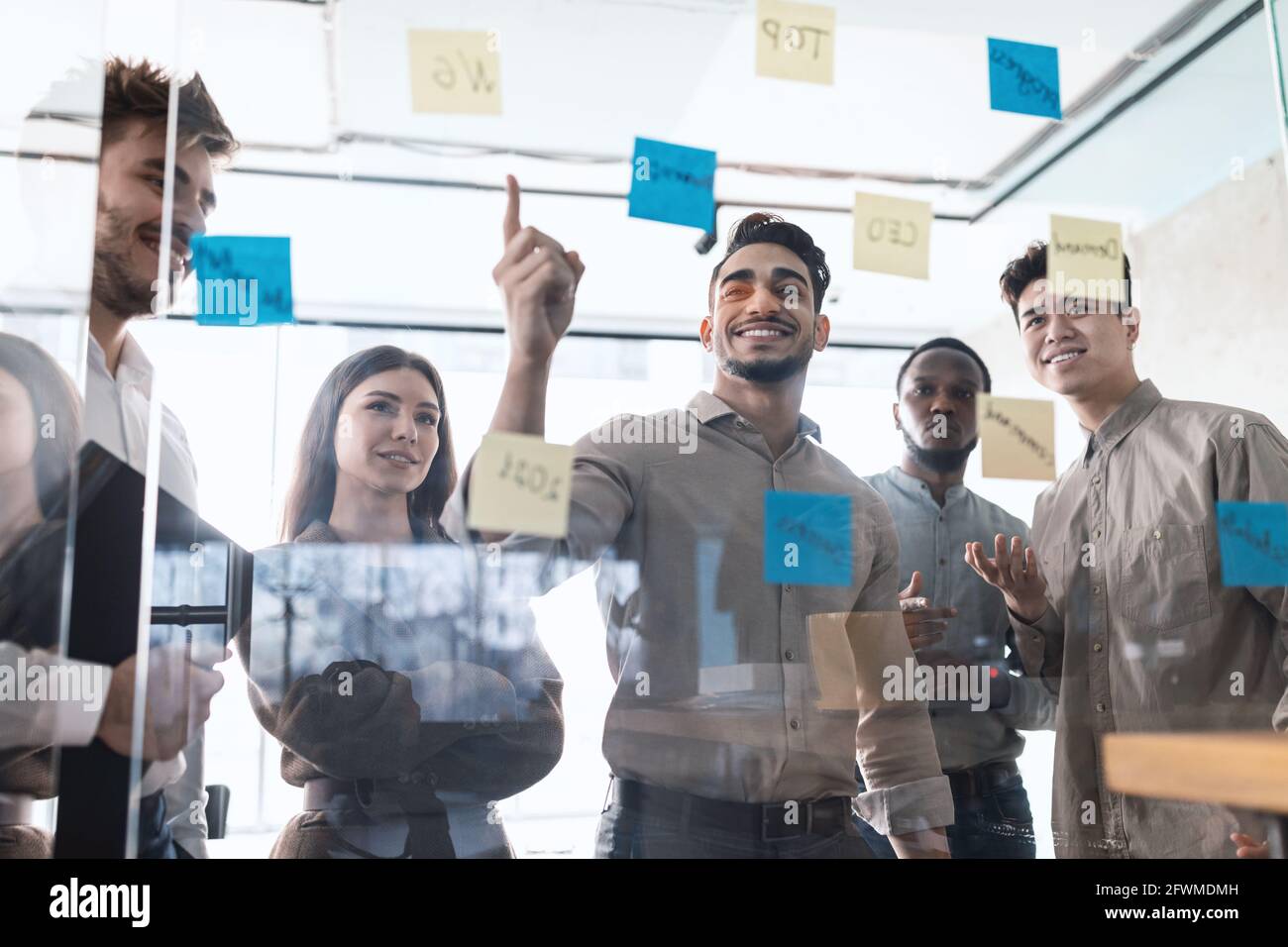 Colleagues having meeting using sticky notes on glass wall Stock Photo