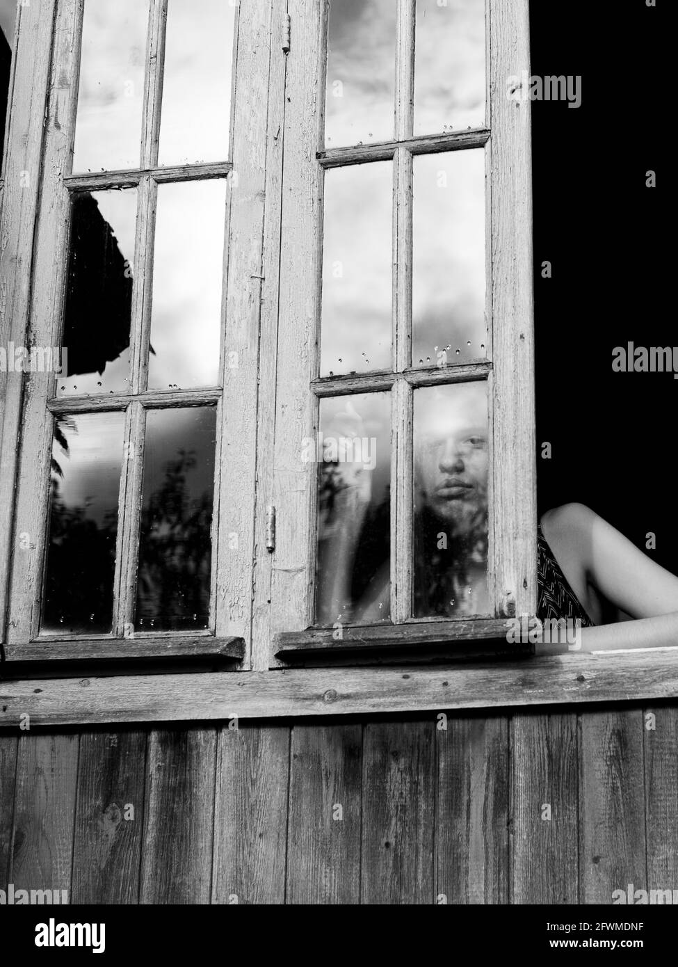 Young woman looks from of the window of the house. Black and white photo. Stock Photo
