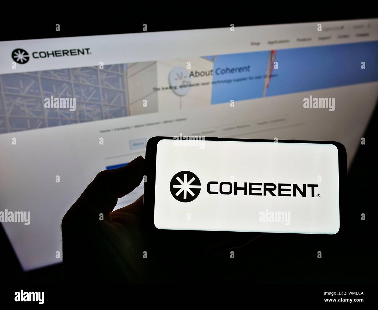 Person holding cellphone with business logo of US laser manufacturer Coherent Inc. on screen in front of company website. Focus on phone display. Stock Photo