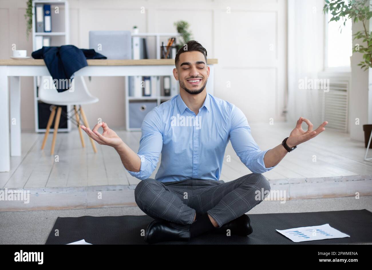 Workplace stress management concept. Calm Arab man meditating with closed eyes, doing yoga at modern office Stock Photo