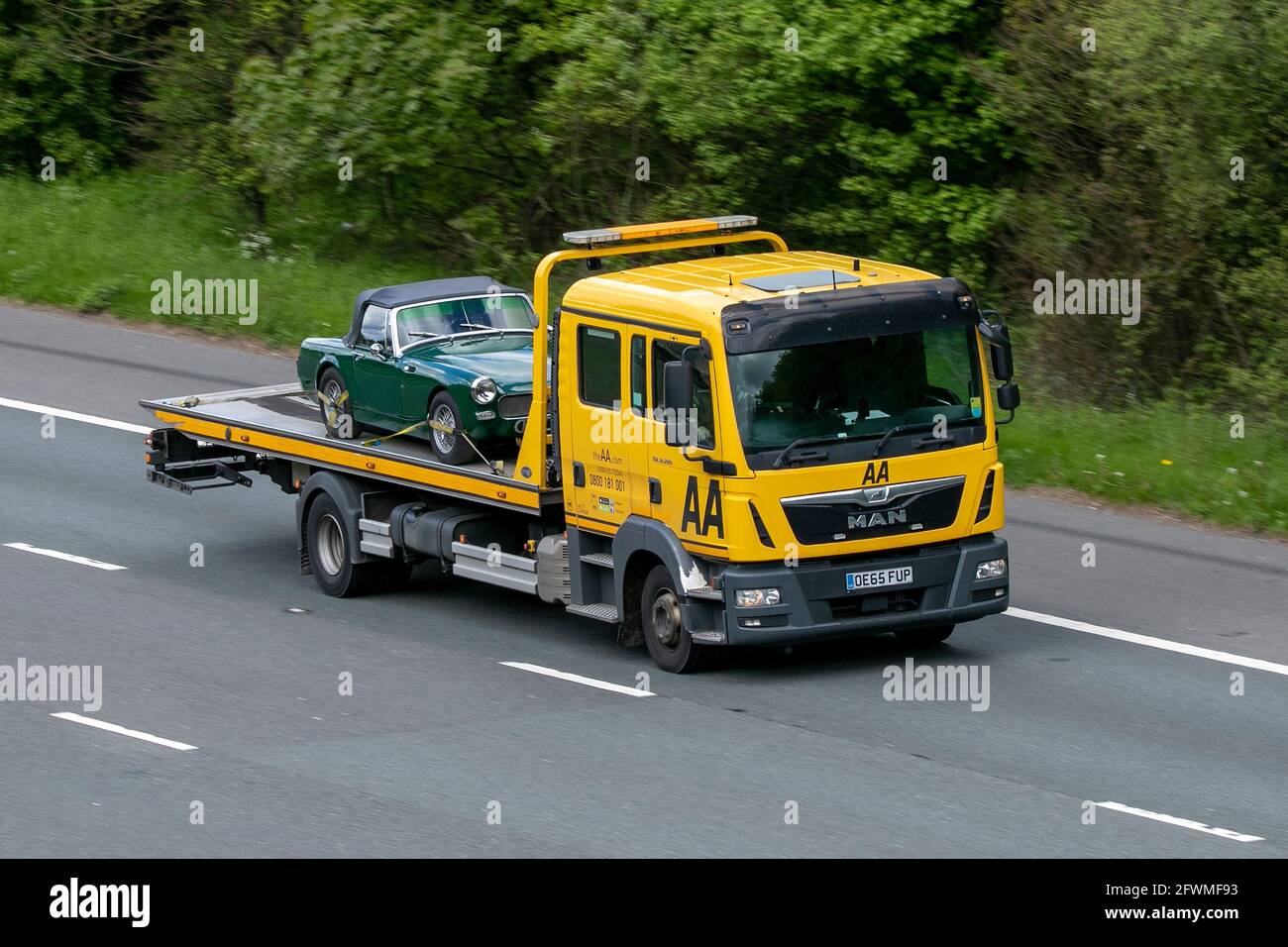 Classic green MG B convertible on AA recovery truck driving on the M6 motorway near Preston in Lancashire, UK Stock Photo