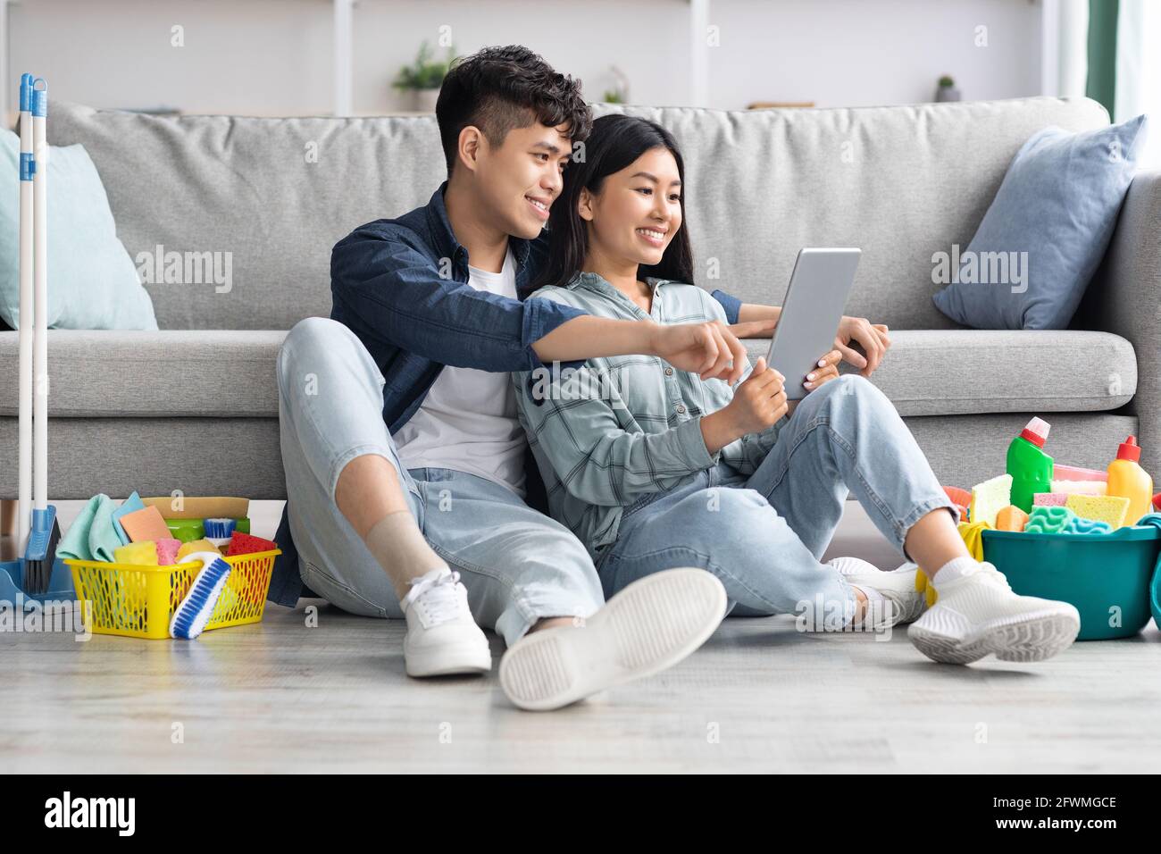 Loving asian couple with cleaning tools resting, using digital tablet Stock Photo